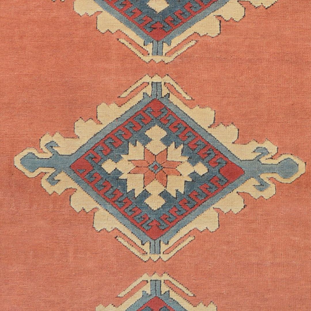 Inspired by traditional Turkish Oushak designs, this handwoven wool rug has a shaded brick red field enclosing a central column of three flourished diamonds, in a beige linked flowerhead border, between tonal blue zig-zag stripes.