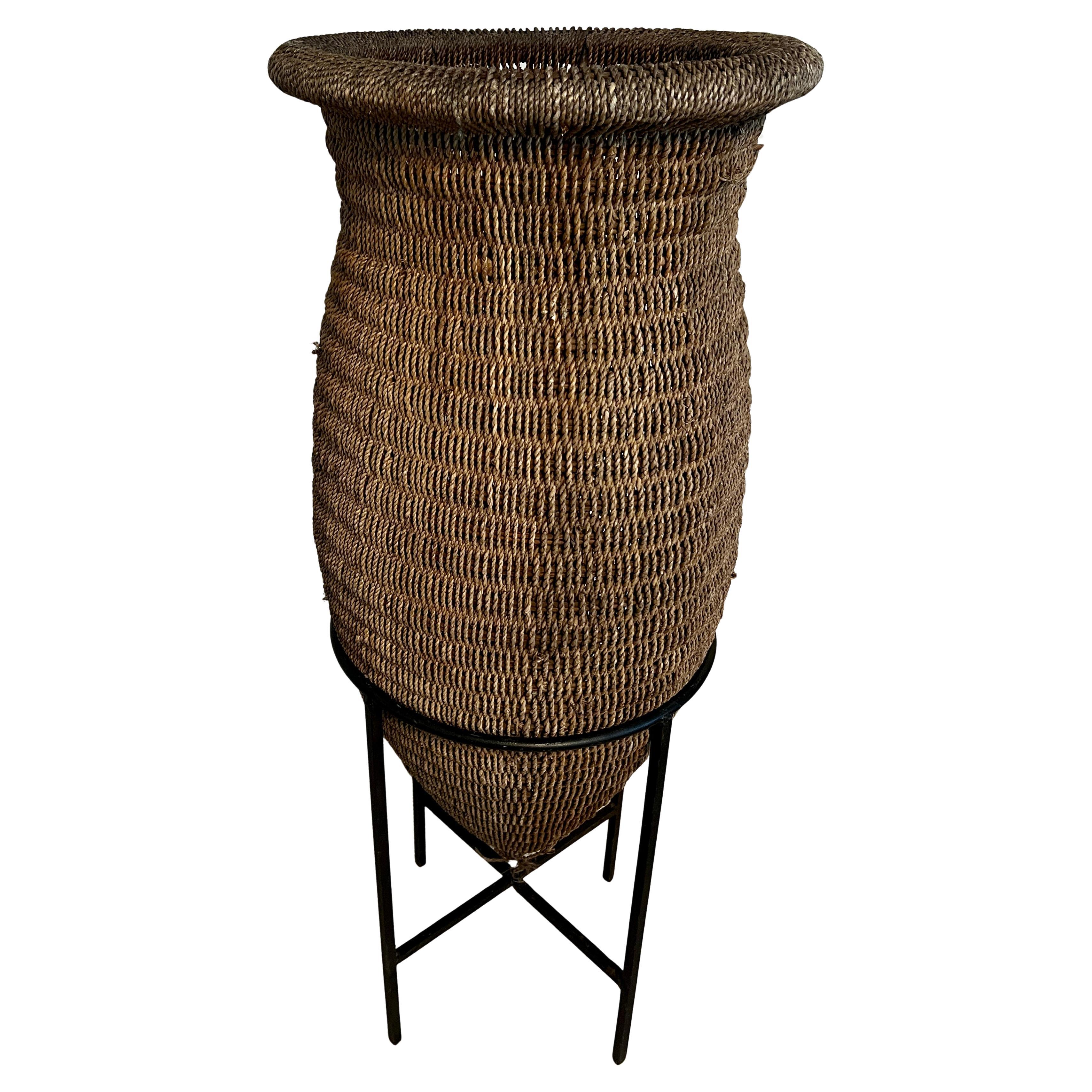 Cesta asiática de ratán tejida a mano sobre soporte de hierro forjado en venta