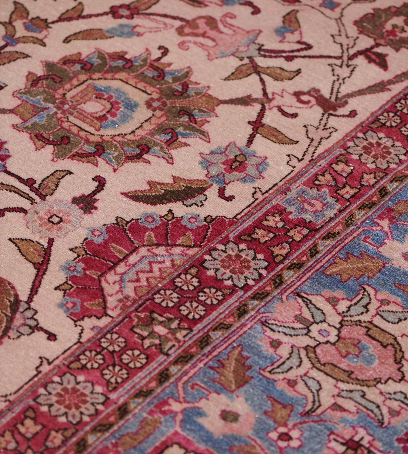 This vintage, circa 1940, Persian Tabriz rug has a shaded ivory field with an overall design of polychrome palmette and floral vine, in a broad light blue border of ivory and burgundy-red palmette and arabesque vine between burgundy-red flowerhead