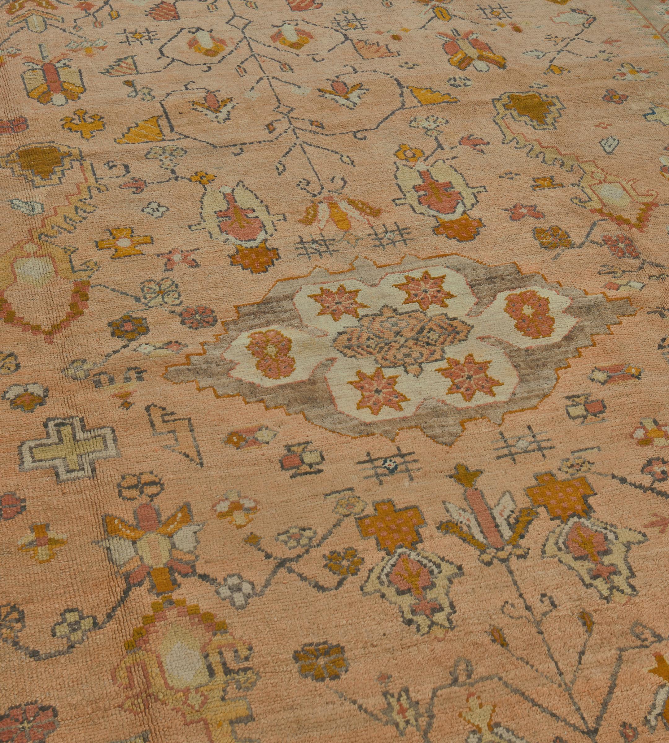 Questo antico tappeto Oushak del 1880 circa ha un campo in terracotta morbida con una losanga centrale avorio e marrone talpa contenente motivi floreali rosso ruggine intorno a una losanga centrale a gradini circondata da fiori angolari e foglie di