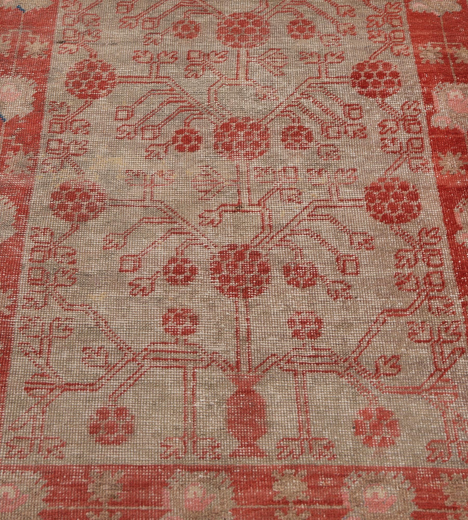 This antique, circa 1890, Khotan runner has a soft-grey field with a coral-red vase at each end issuing a pomegranate and angular leafy and floral vine, in a coral-red border of buff-brown and dusty-pink linked flowerheads alternating with paired