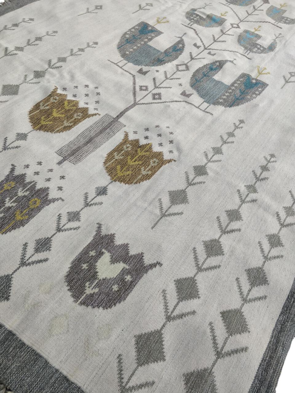 Handgewebter Woll-Kilim (Wandteppich). Design auf hellem Hintergrund mit stilisierten Vögeln und Tulpen, mit sanften Farben in Hellblau und Braun. In der rechten unteren Ecke das Monogramm der Künstlerin N E Eva Nemeth. Aus den 1970er Jahren.
Das