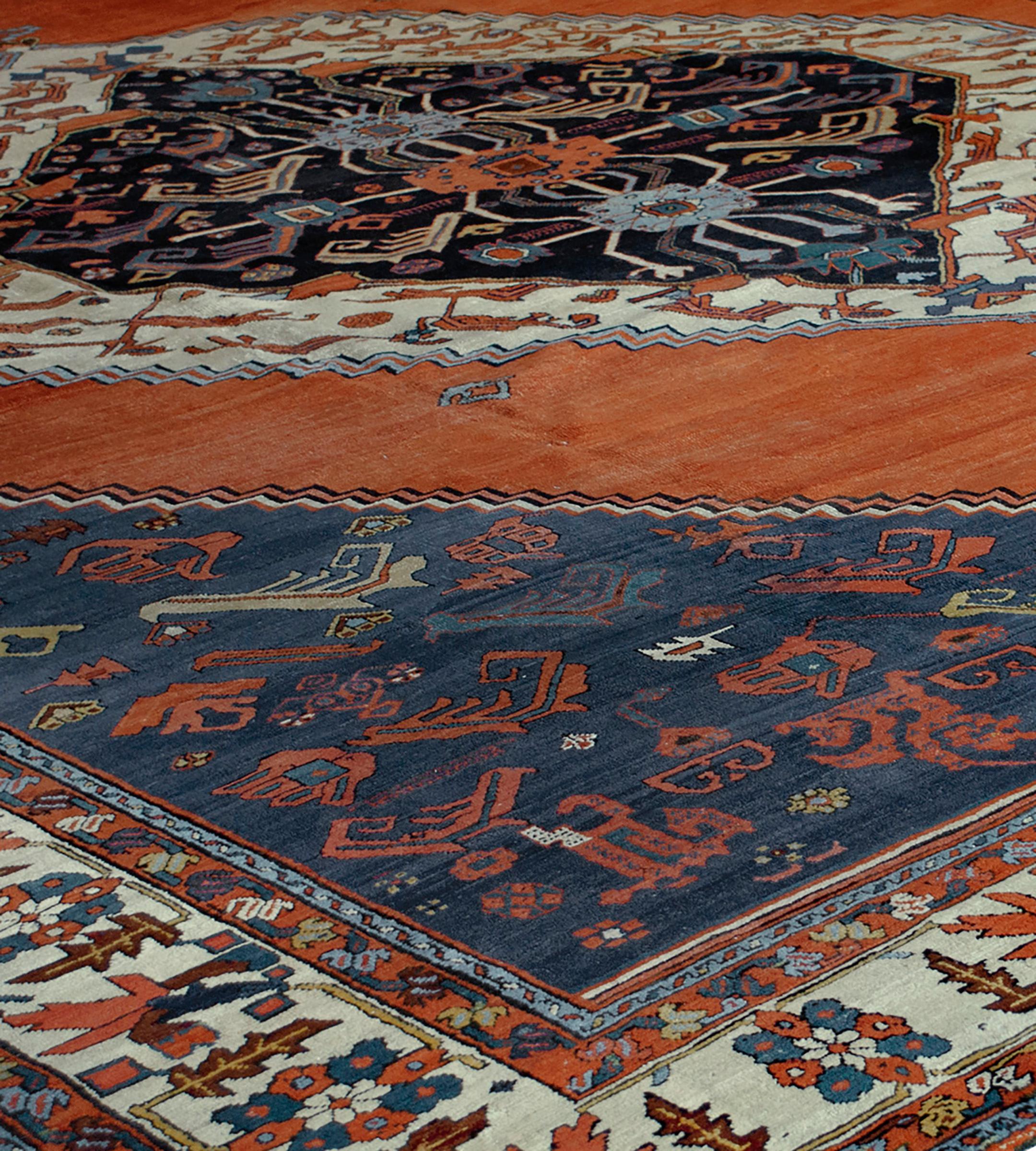 Ce tapis traditionnel serapi persan tissé à la main présente un magnifique champ rubis strié entourant un médaillon en losange bicolore ivoire/charbon de vignes et de rosettes stylisées, avec des écoinçons marine nuancés similaires, dans une bordure
