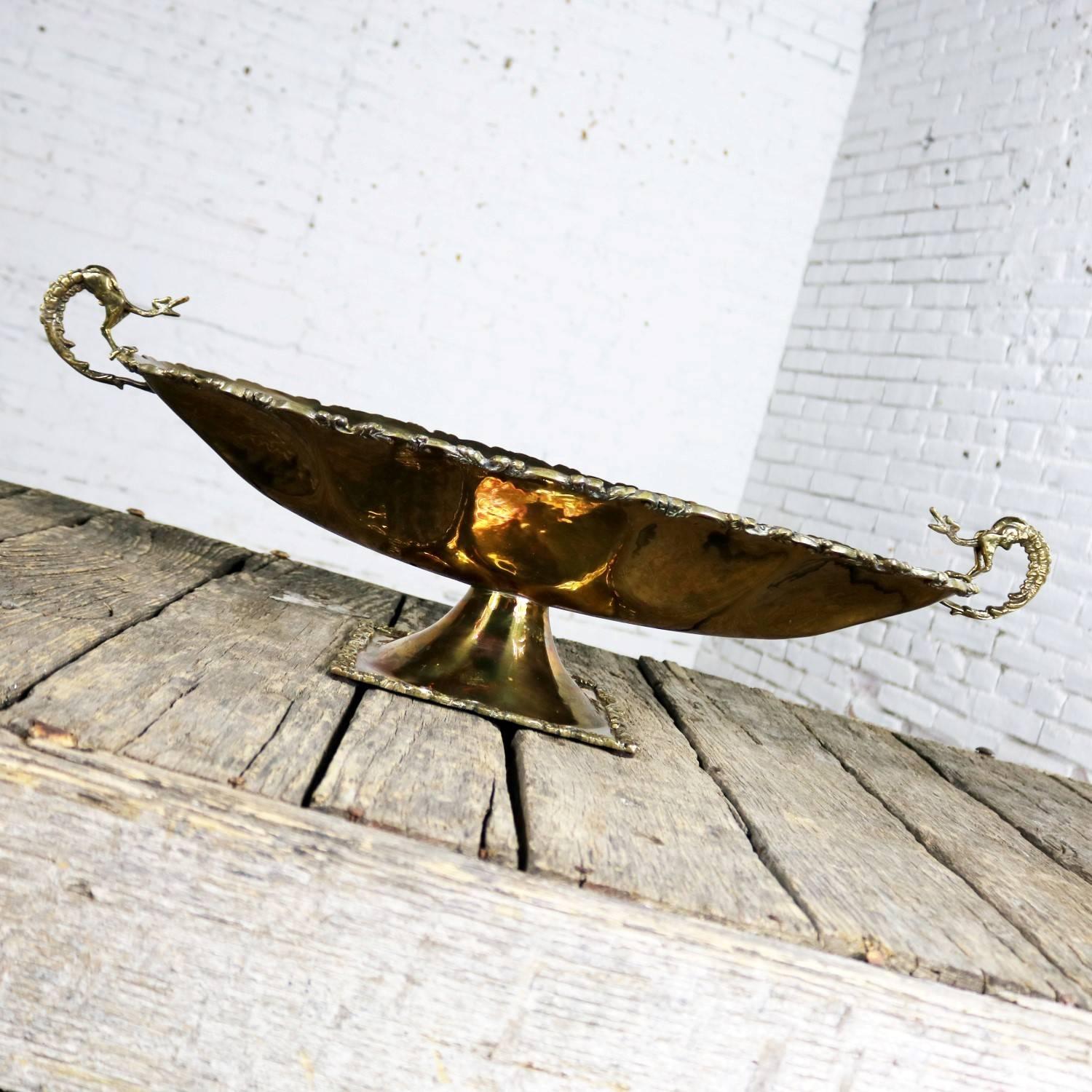 Gorgeous monumental brass centerpiece with oval bowl in a footed compote style. It is hand-wrought with cast brass details and dragon handles. In wonderful vintage condition and with a natural patina to its finish, circa 1950s-1960s.

Just look at