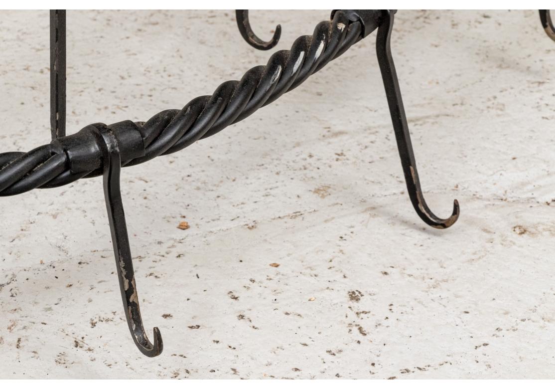 A well crafted black hand wrought two tiered iron hanging pot rack with 24 hooks. The rack with a spiral twist motif having a smaller oval tier conjoined with acanthus leaf motifs above a larger tier, 12 hooks each. The rack comes with four brackets