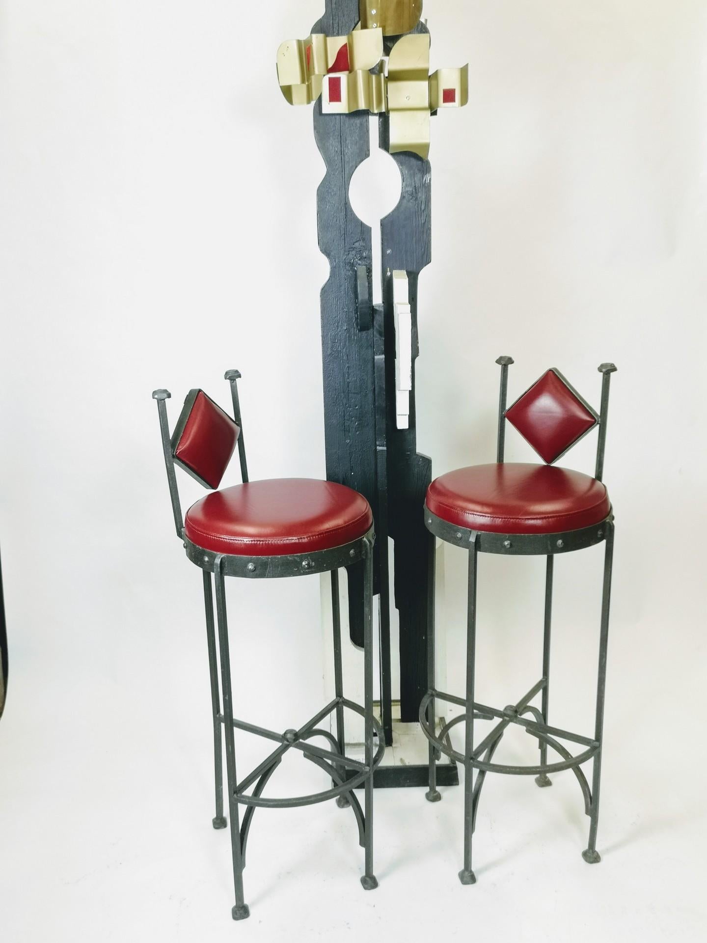 These hand-hammered and handwrought iron bar stools feature brand new cushioning and a dark red/maroon leather upholstery. They're a pair of 1970s vintage pieces.
