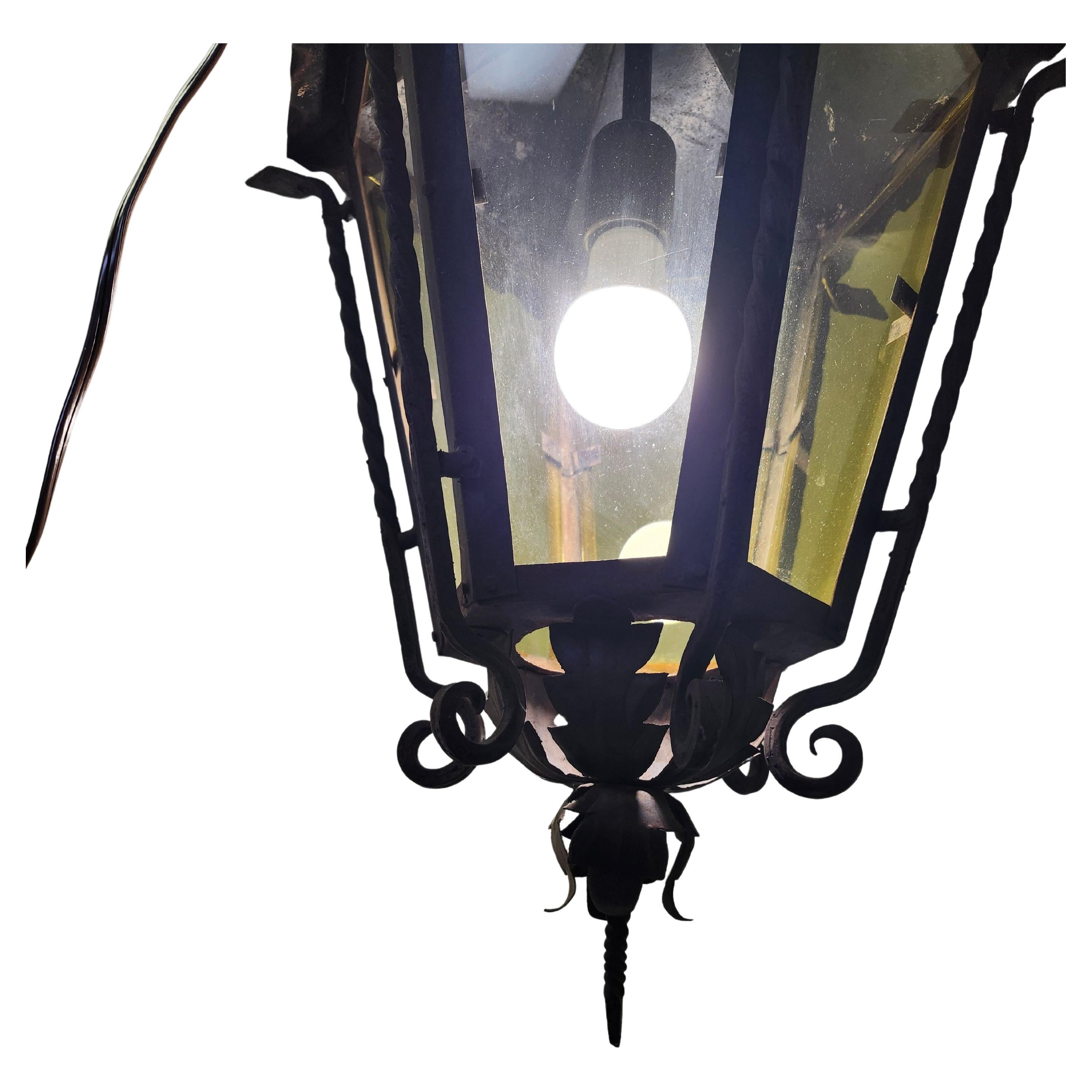 Fantastique lustre suspendu d'extérieur simple et élégant, forgé à la main, avec verre teinté jaune.  
Des spirales, des rosettes et des feuilles d'acanthe travaillées à la main ornent la lampe. En peinture noire d'origine qui pourrait être