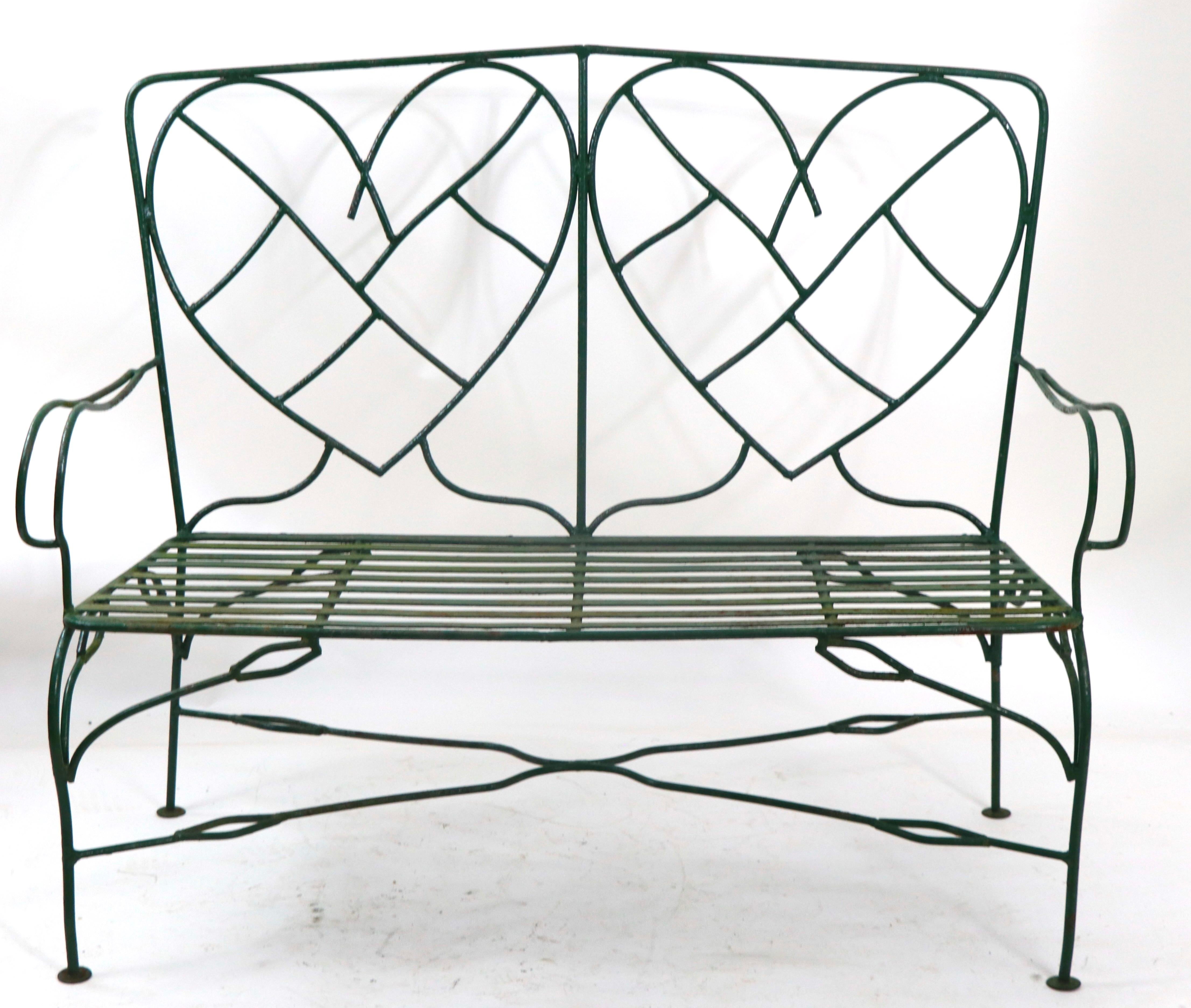 Exceptional, charming and romantic hand wrought iron settee, loveseat, bench, in very fine, original condition. The bench features a heart motif back rest, adding to the romantic feel of this unusual and possibly unique vintage bench. Perfect for