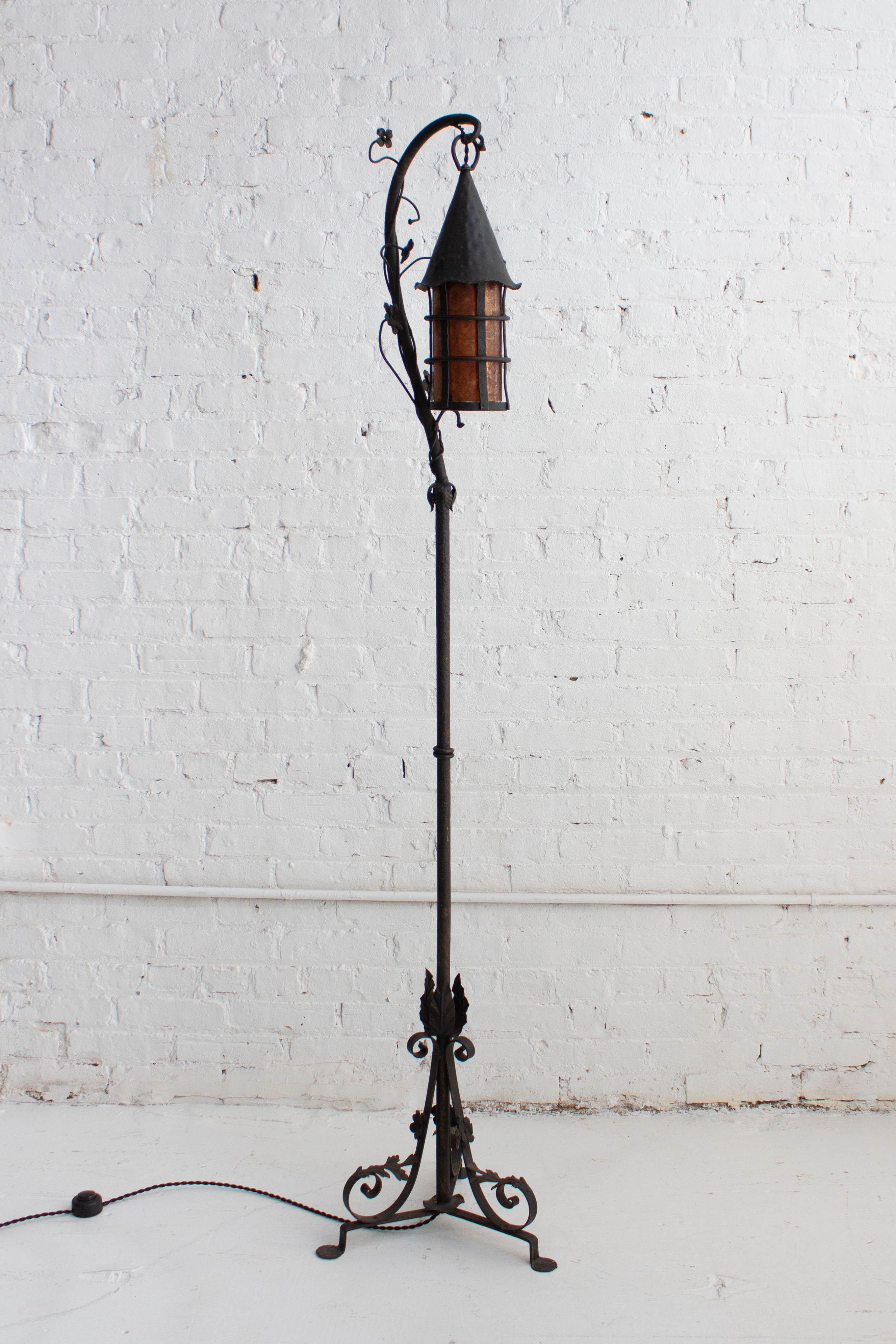 A hand-wrought iron floor lamp in the style of Oscar Bach. In the Tudor revival style with whimsical floral details. Mica insert shade provides a warm glow. Floor foot on / off switch. Pair available, sold individually.