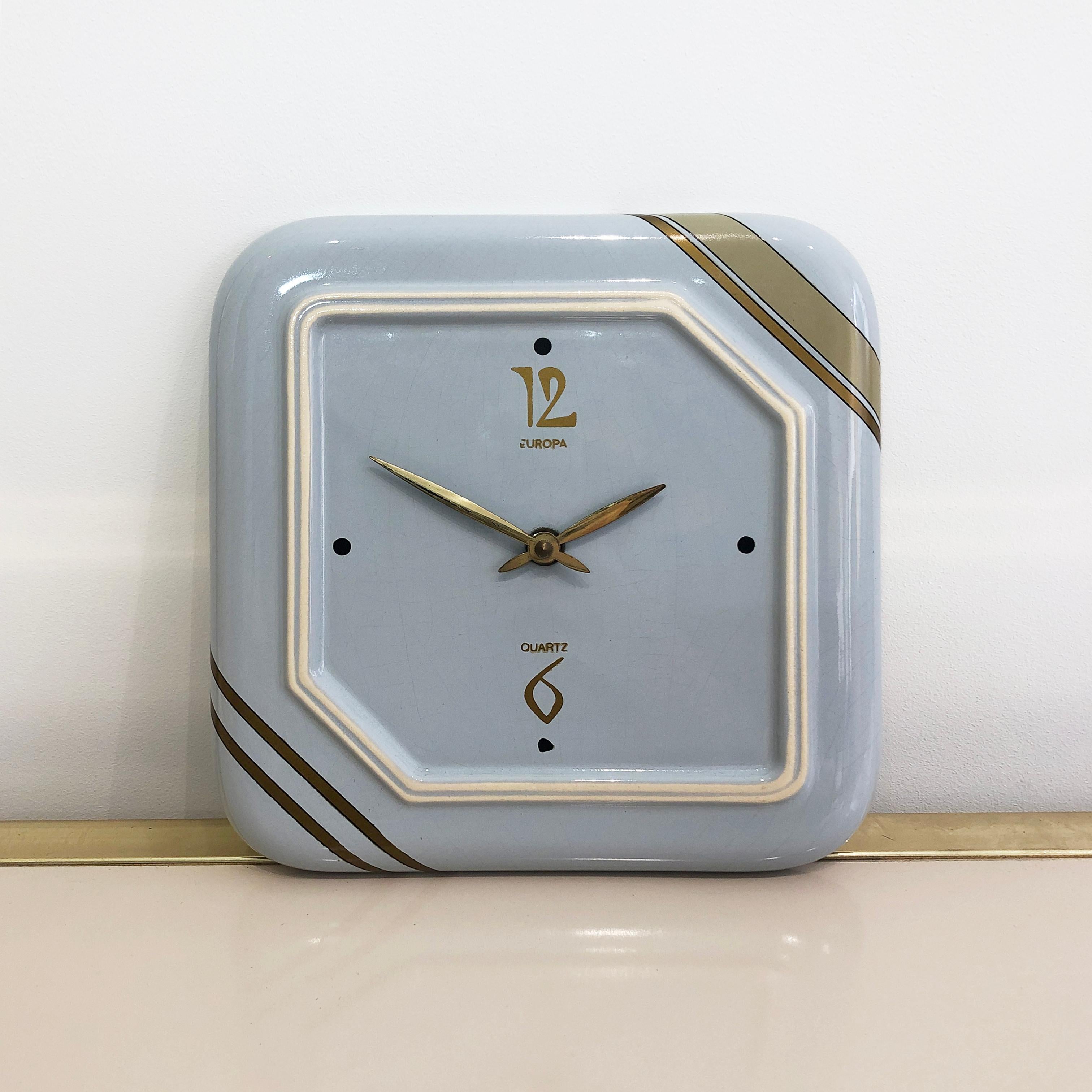 Finished with gold leaf and a Classic blue pastel colour, this square ceramic wall clock, marked “Handarbeit 42154”, is a fine example of midcentury West German craftsmanship. 

Minimal, and with a rustic elegance, this timepiece would be an