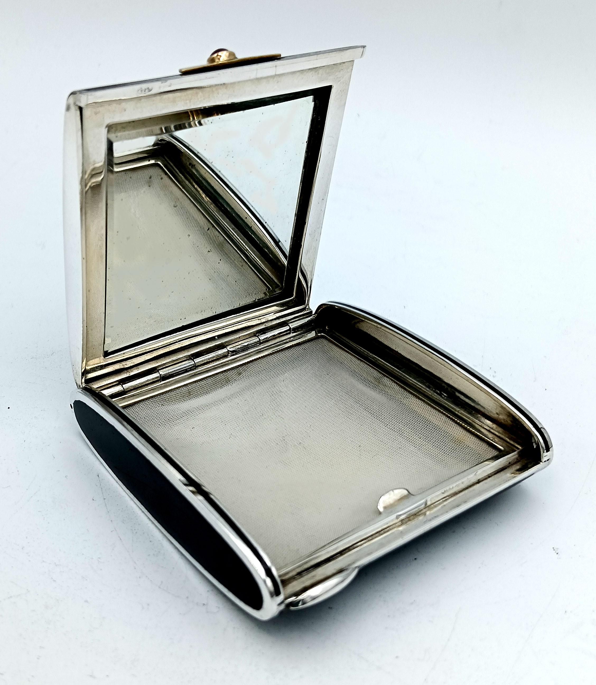 Portacipria da borsetta a sezione ovale in argento 925/1000 con smalto nero cotto. Apertura con lunetta in oro 18 carati con rubino cabochon rotondo, diametro 4 mm. Specchio a terra leggermente macchiato a causa del tempo trascorso e rete