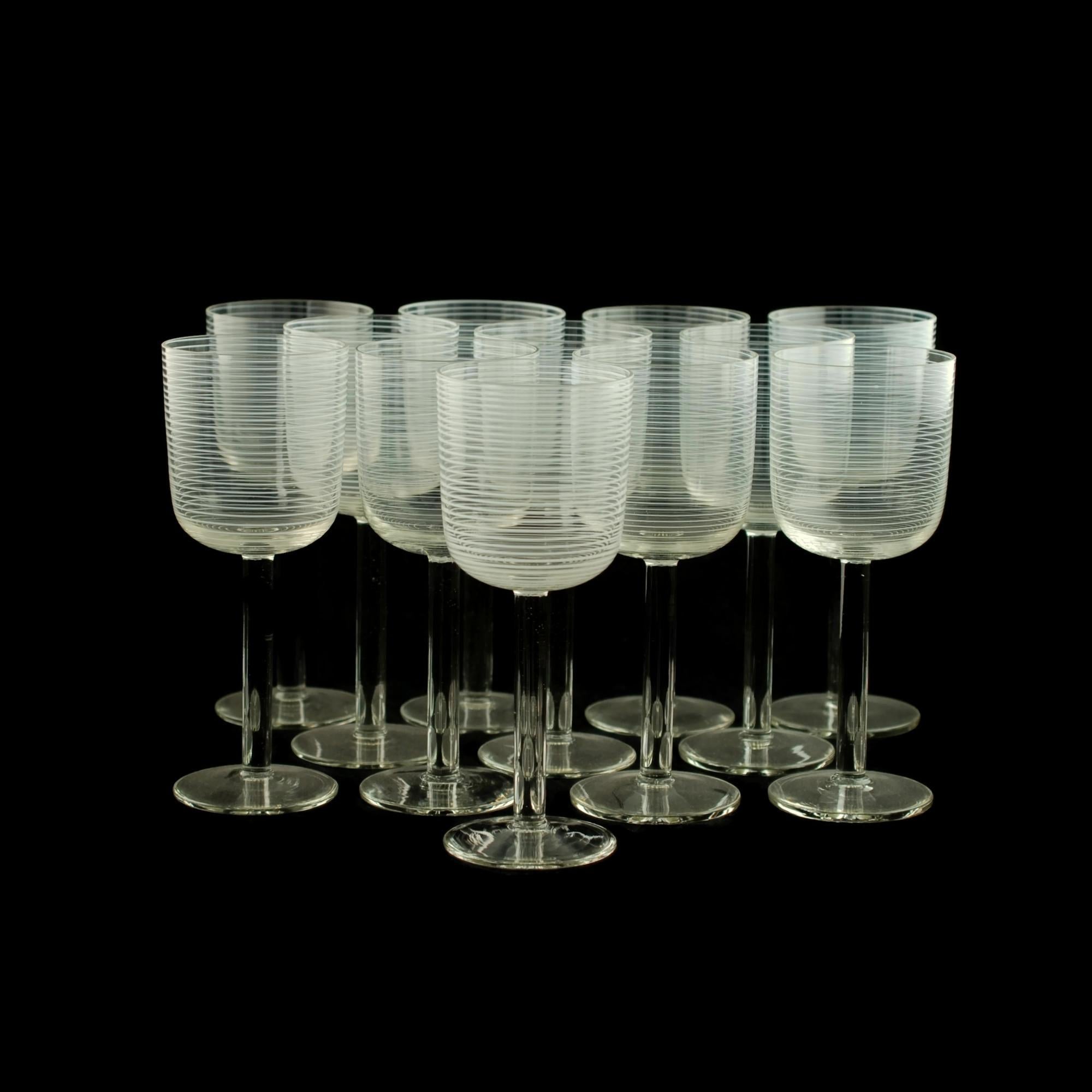 Cet élégant ensemble de 12 gobelets en cristal clair soufflé à la bouche présente des bols décorés de fils de verre blanc opaque. Les fils partent du fond des bols et s'enroulent en spirale autour de l'extérieur, formant une série de nervures