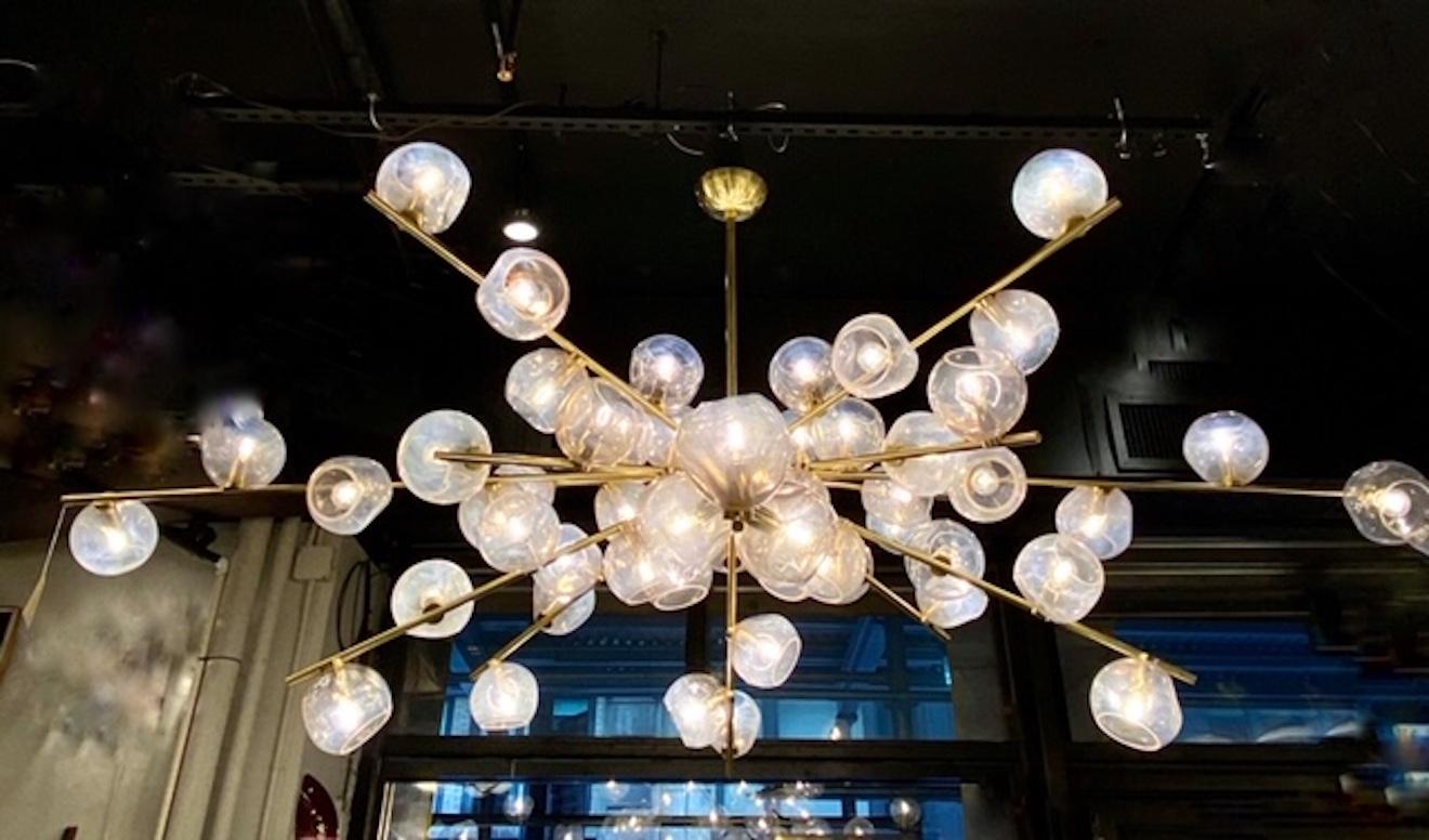 This stunning and monumental modernist chandelier is hand blown and handcrafted. It features an abundance of organic hand blown iridescent shades- each uniquely formed- attached to brass arms that appear to 