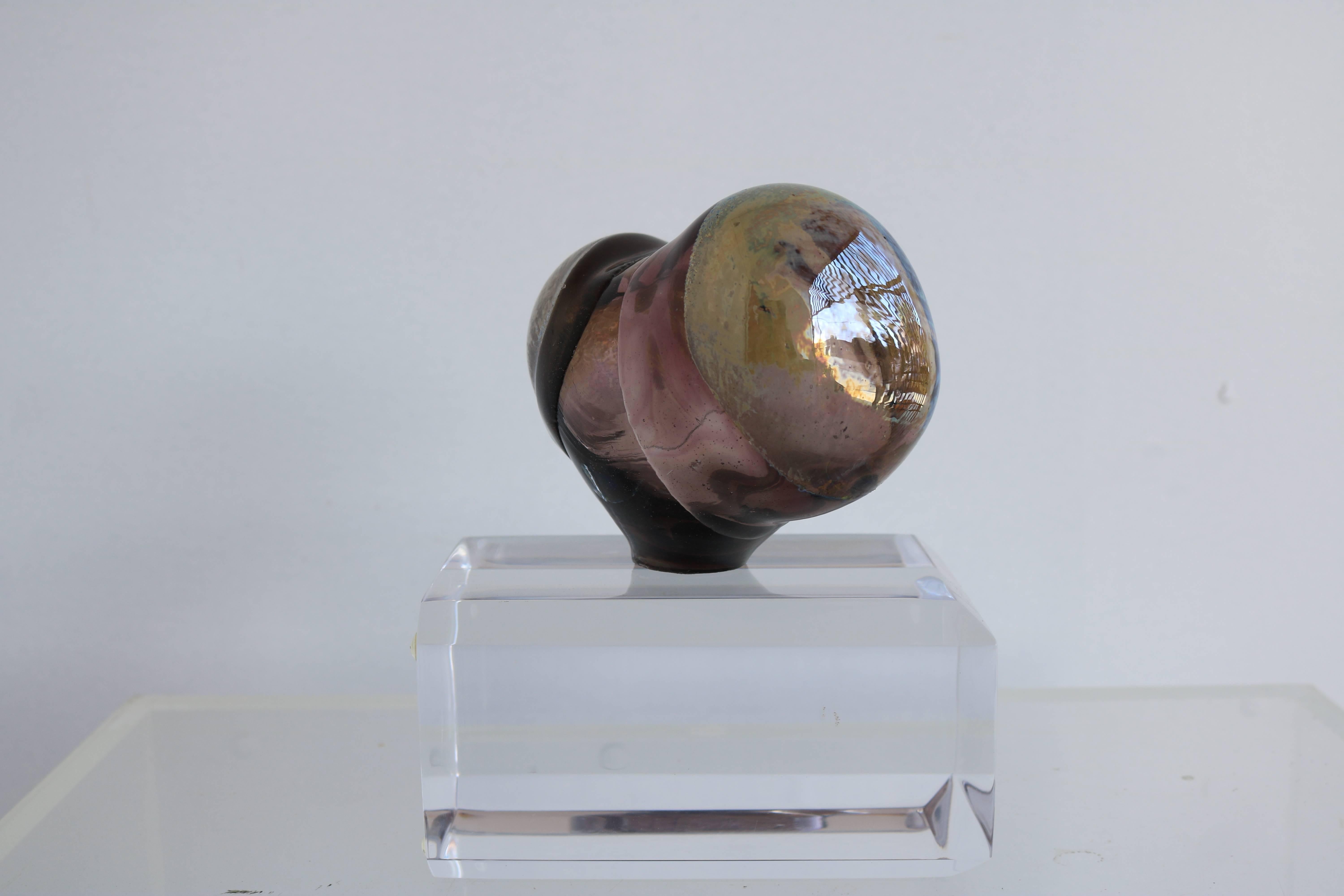 This petite glass bud sculpture is made from violet-tinted blown glass in the shape of a mushroom cloud. There is a tiny hole in the top, as pictured, large enough for one-two flower stems. The underside is illegibly signed. Displayed on a plexi