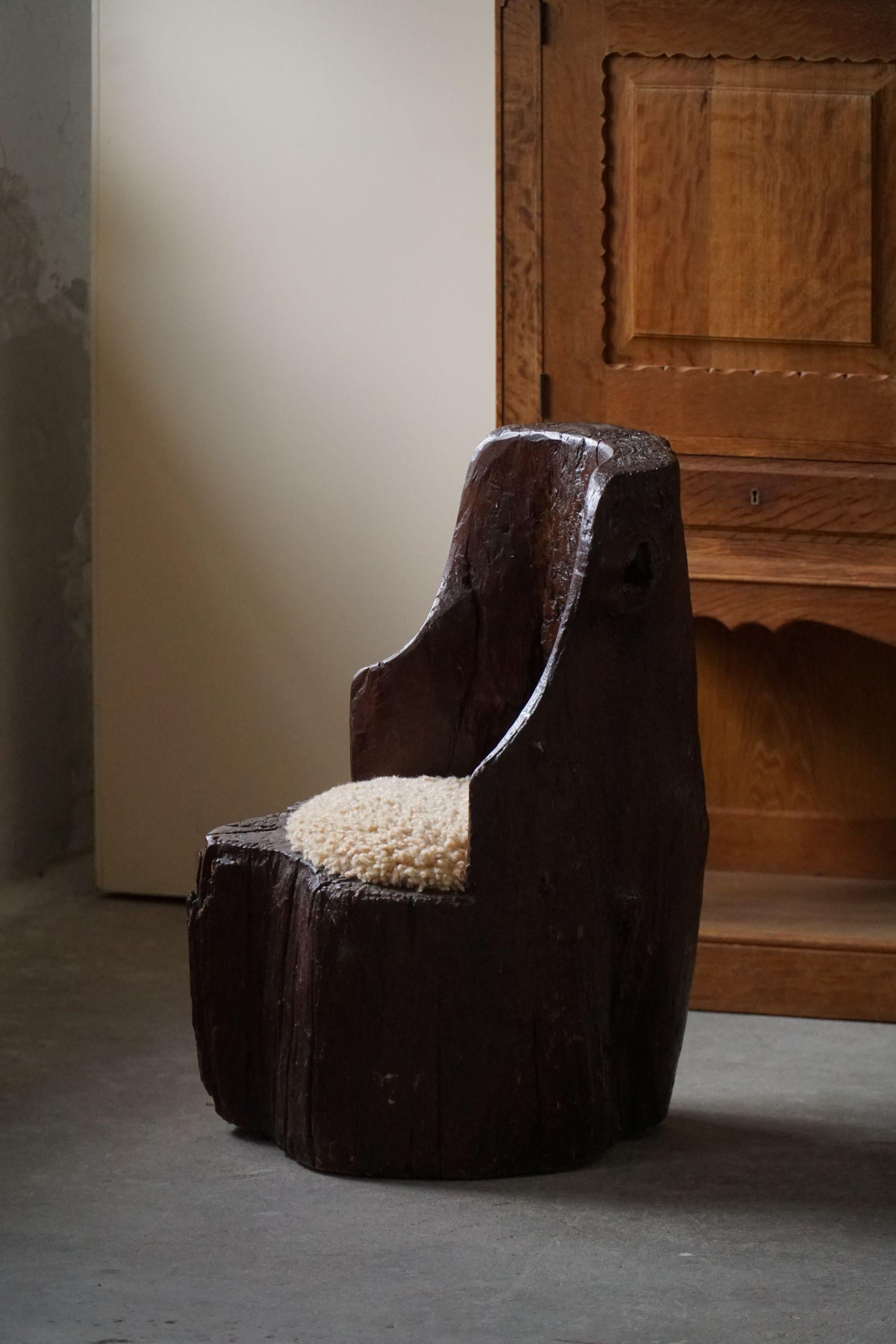 Une authentique chaise de souche primitive fabriquée en une seule pièce de bois massif. Siège retapissé en laine d'agneau shearling de grande qualité. 
Sculpté à la main par un ébéniste suédois au début du XXe siècle. Une pièce unique et lourde de