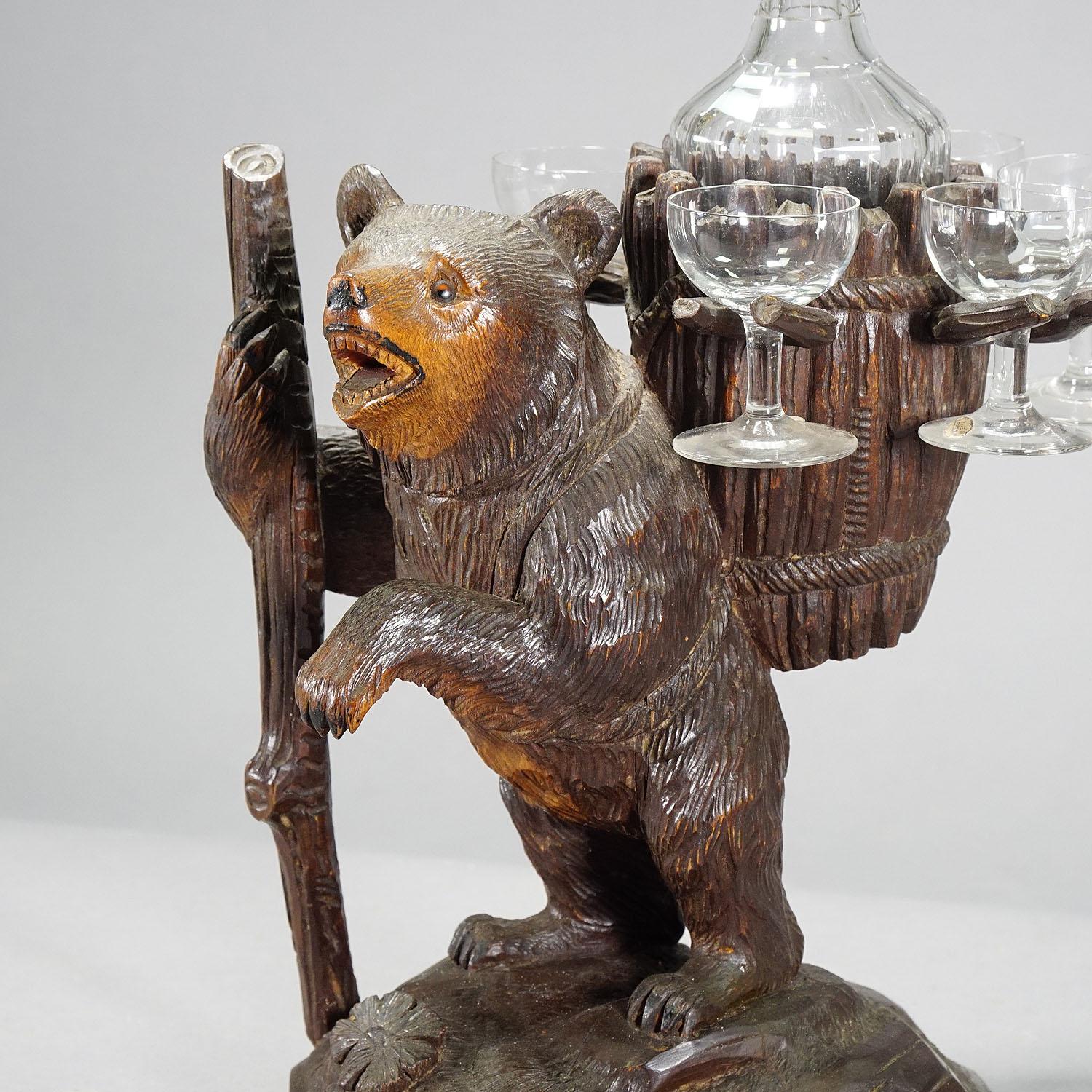 A carved wood decanter / liqueur stand modelled as hiking bear with walking stick and basket on his back. With cutted glass decanter and six glasses. Executed, circa 1920, Swiss. (Height bears only)

Measures: Width 7.87