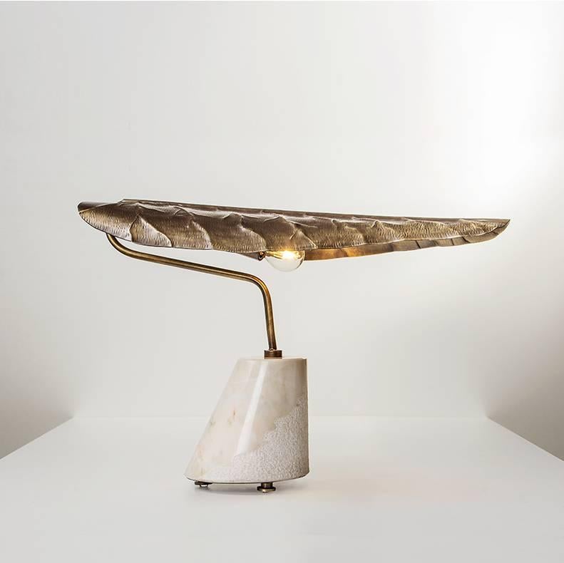 Estremoz cream colored marble based table lamp with hand etched and burnished brass calla lily leaf shaped lampshade. The hammered and aged brass shade connects to the marble base in a slender form, shaped like the neck of a resting swan. 
Galerie