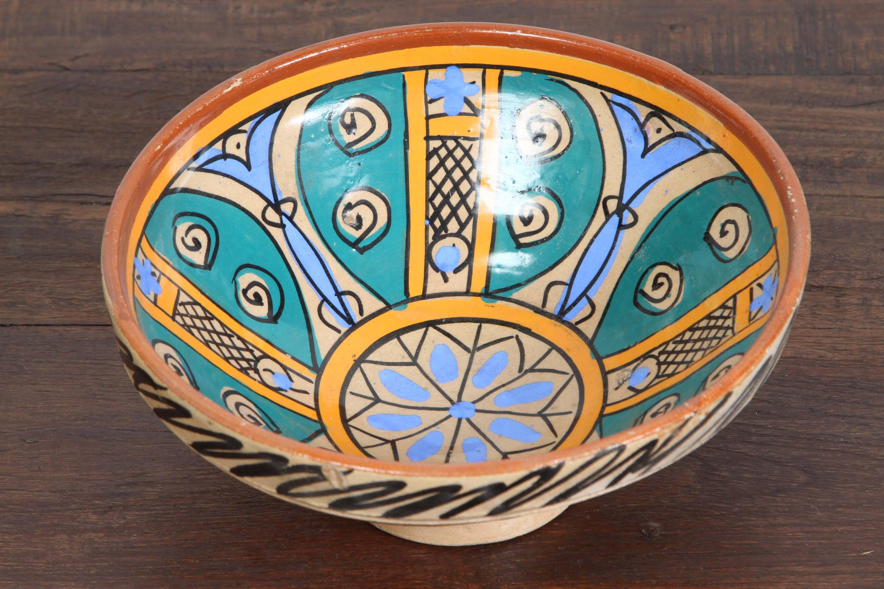 An under-glazed painted pottery bowl with abstract naive design, blue, ochre, brown.
Moroccan antique pottery bowl of deep rounded form with flattened rim rising on a low ring foot, hand-painted on the exterior with black decoration, the interior in