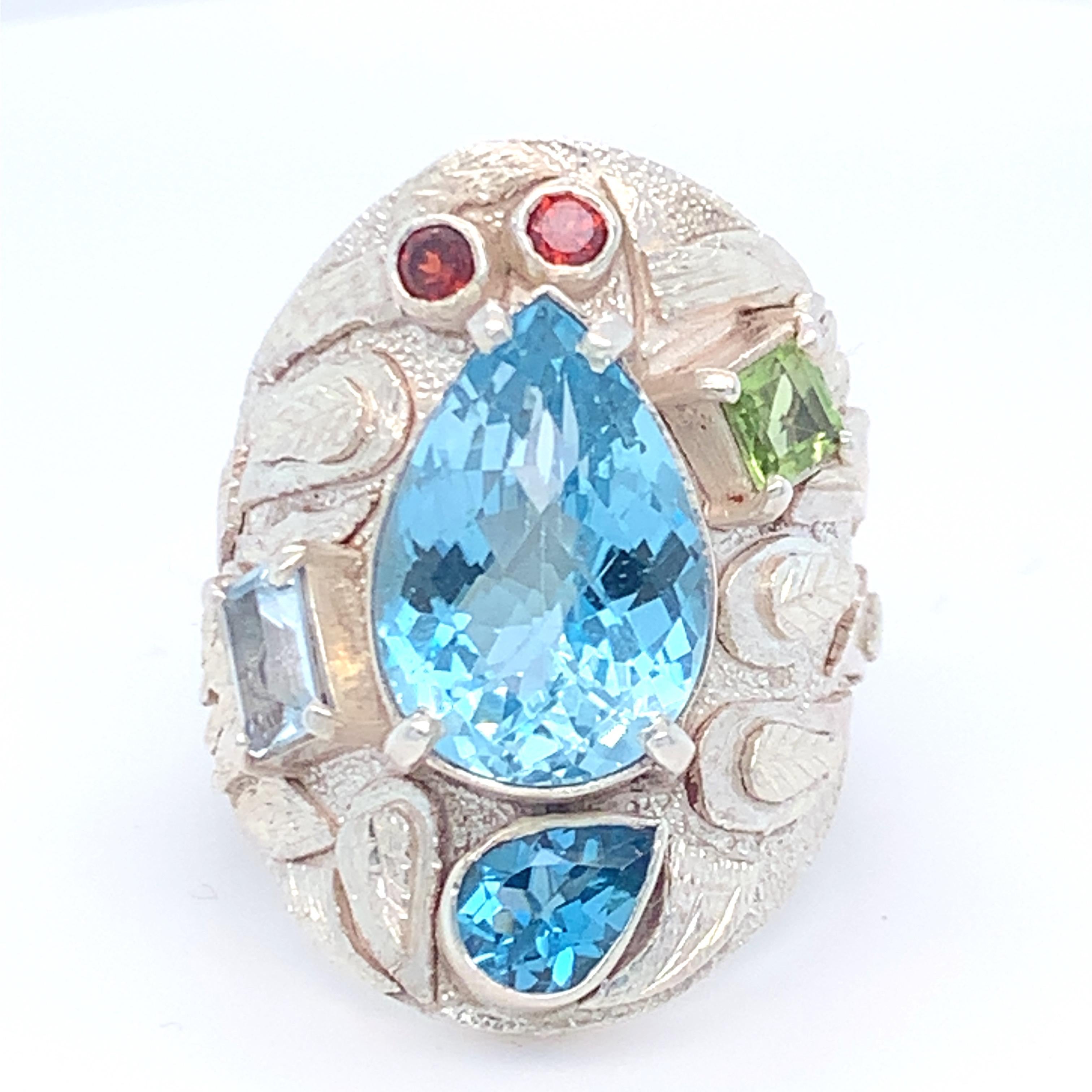 Tear drop Blue Topaz is the main stone of this stunning cocktail ring. Accent stones of peridot, garnet, aquamarine and blue topaz are placed asymmetrically around the main stone which enhances the beauty of this ring. Set in sterling silver and