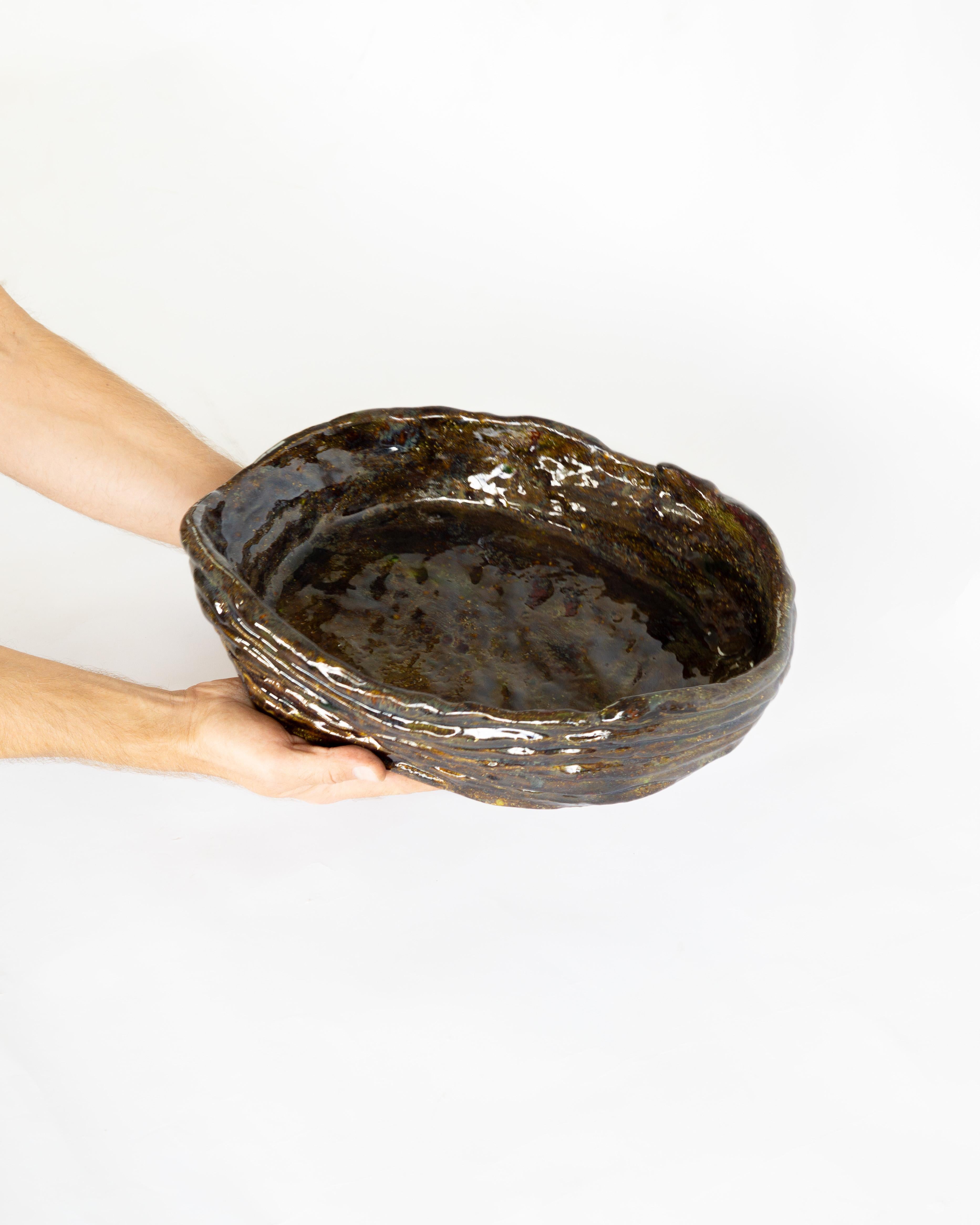 Ce bol en céramique artisanale est fabriqué selon la technique traditionnelle du serpentin et présente une palette chaude et terreuse de tons bruns et verts. Sa forme organique, avec des murs légèrement incurvés et une structure en serpentin