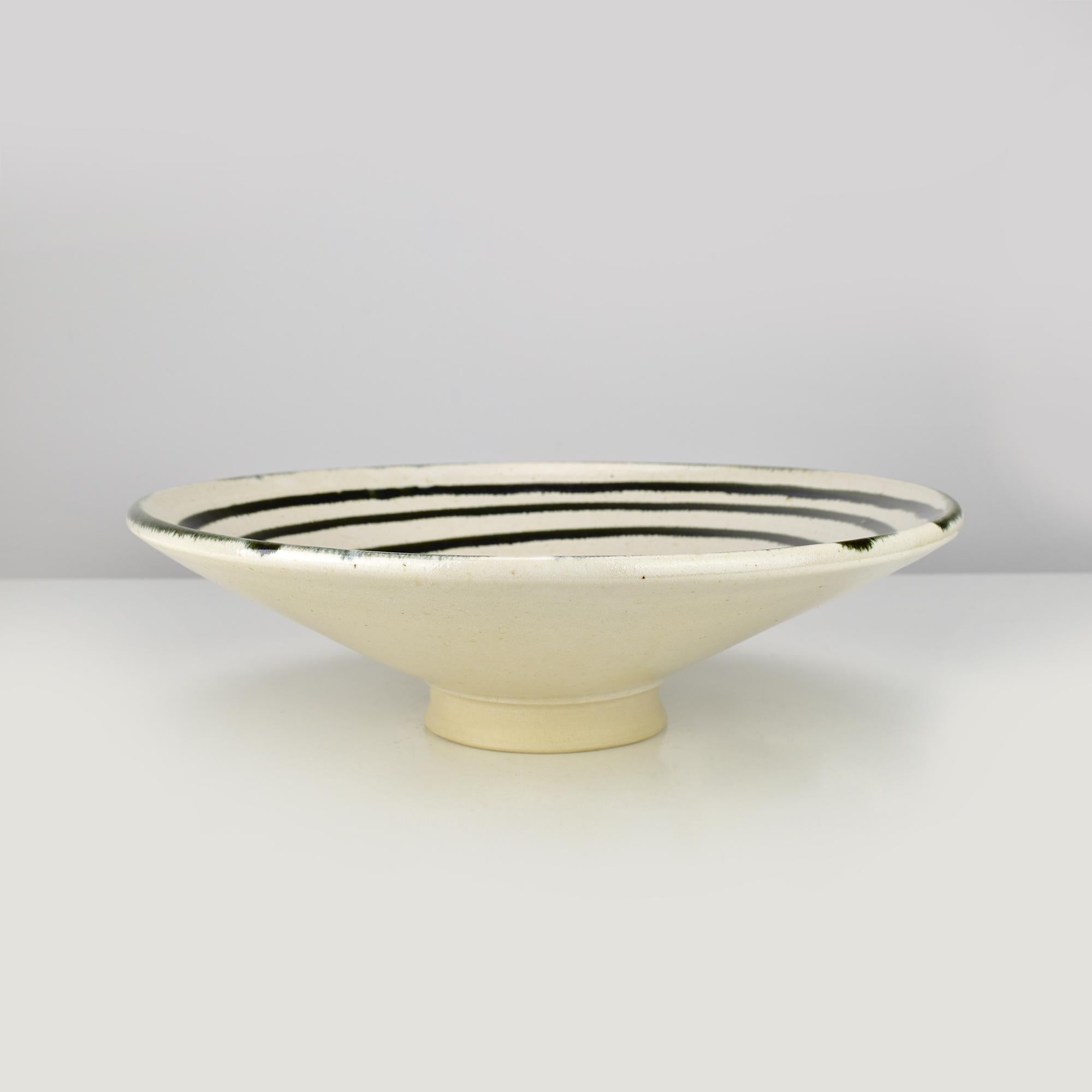 Este cuenco de cerámica artesanal presenta un llamativo diseño en espiral negra sobre esmalte blanco. La decoración minimalista pero atrevida se combina con una refinada forma poco profunda y un pie elevado, lo que confiere a la pieza un aspecto