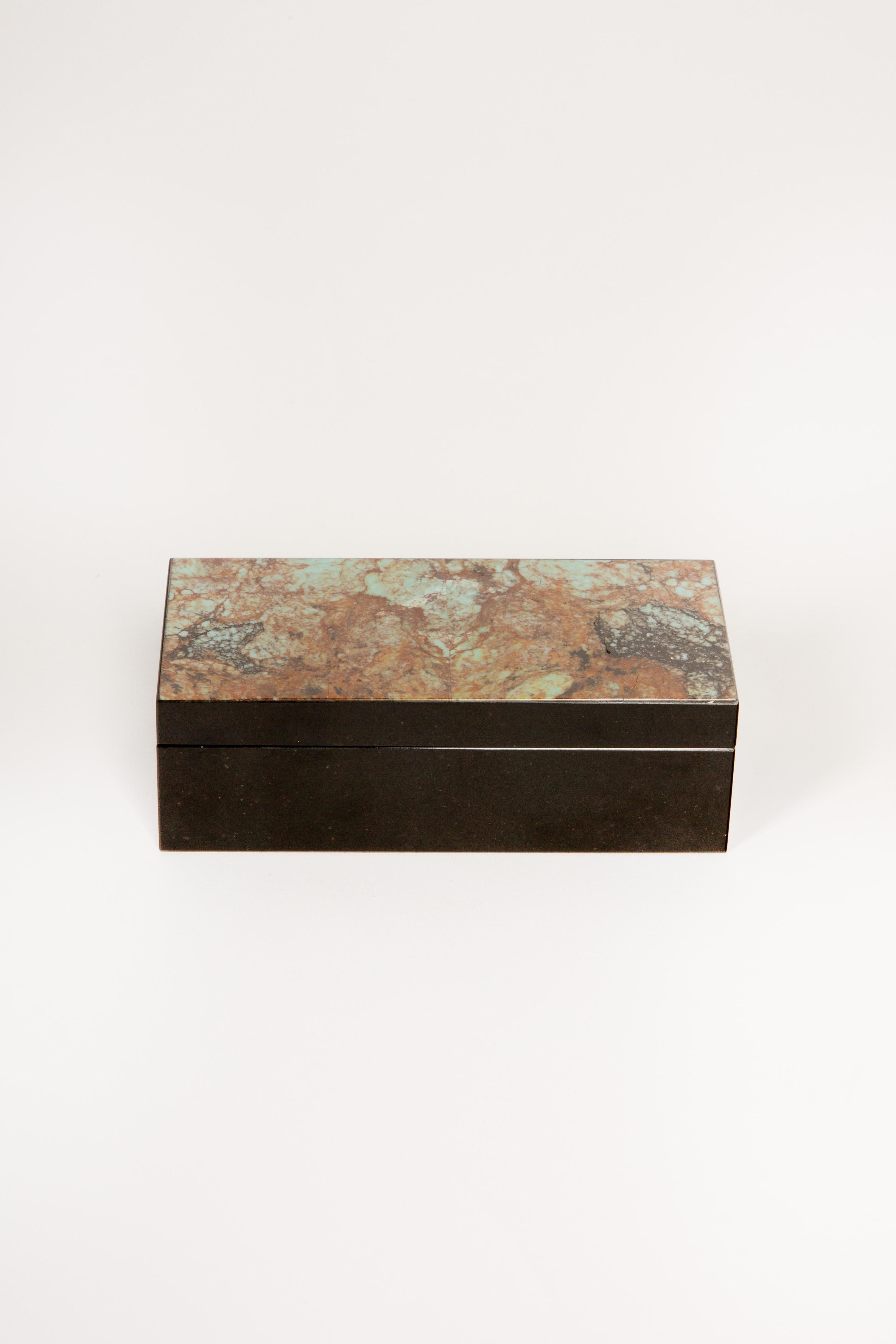 Esta exquisita caja artesanal presenta una impresionante tapa con incrustaciones de crisocola, que exhibe una fascinante mezcla de marrones, azules y verdes terrosos, complementada con una elegante base de ónice negro pulido. El diseño con bisagras,