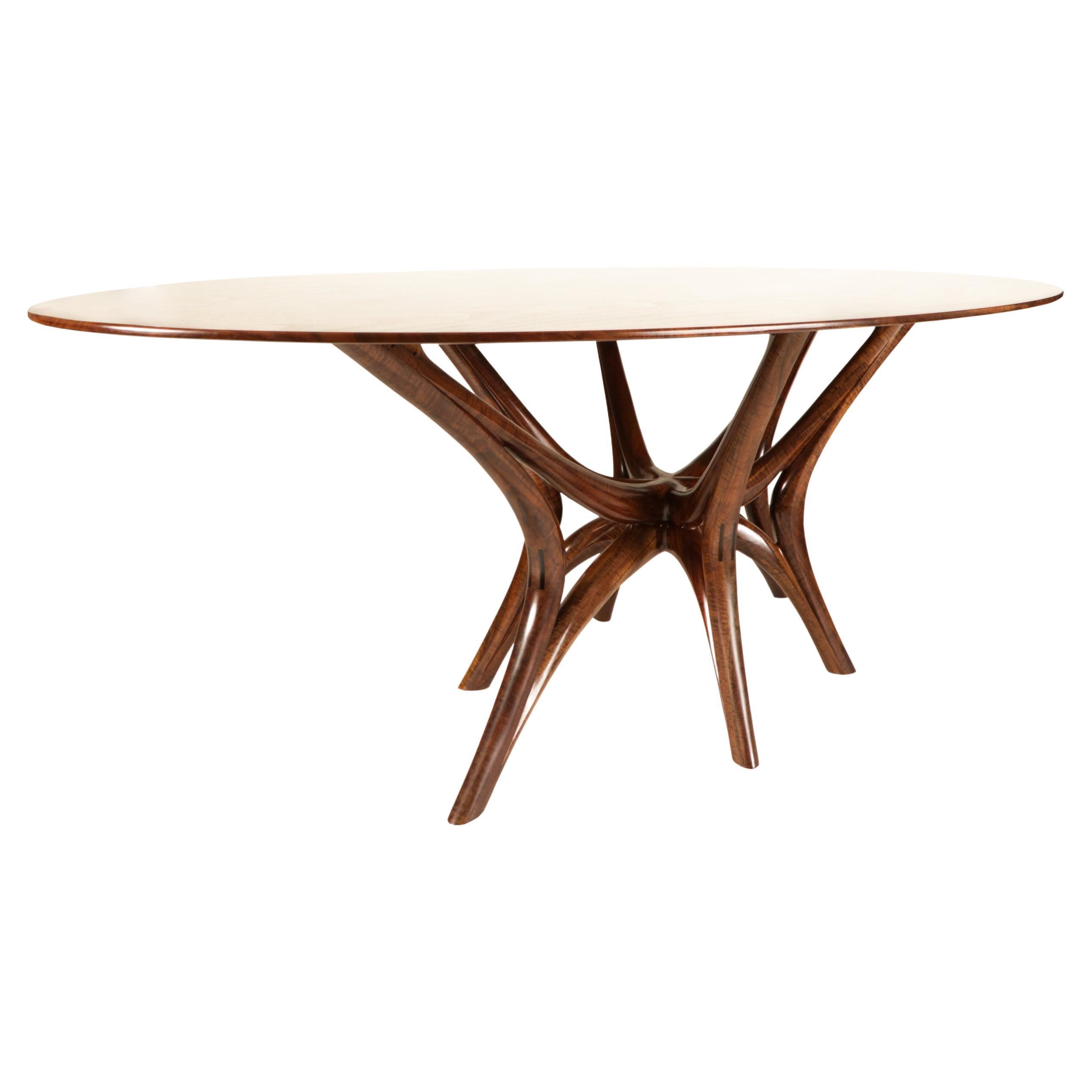 Handcrafted from solid Walnut, this web-leg dining table is a statement in craft and design. It's hand-carved legs offer an incredible sense of movement and the tapered profile of the table top makes it appear to almost be floating in space. This