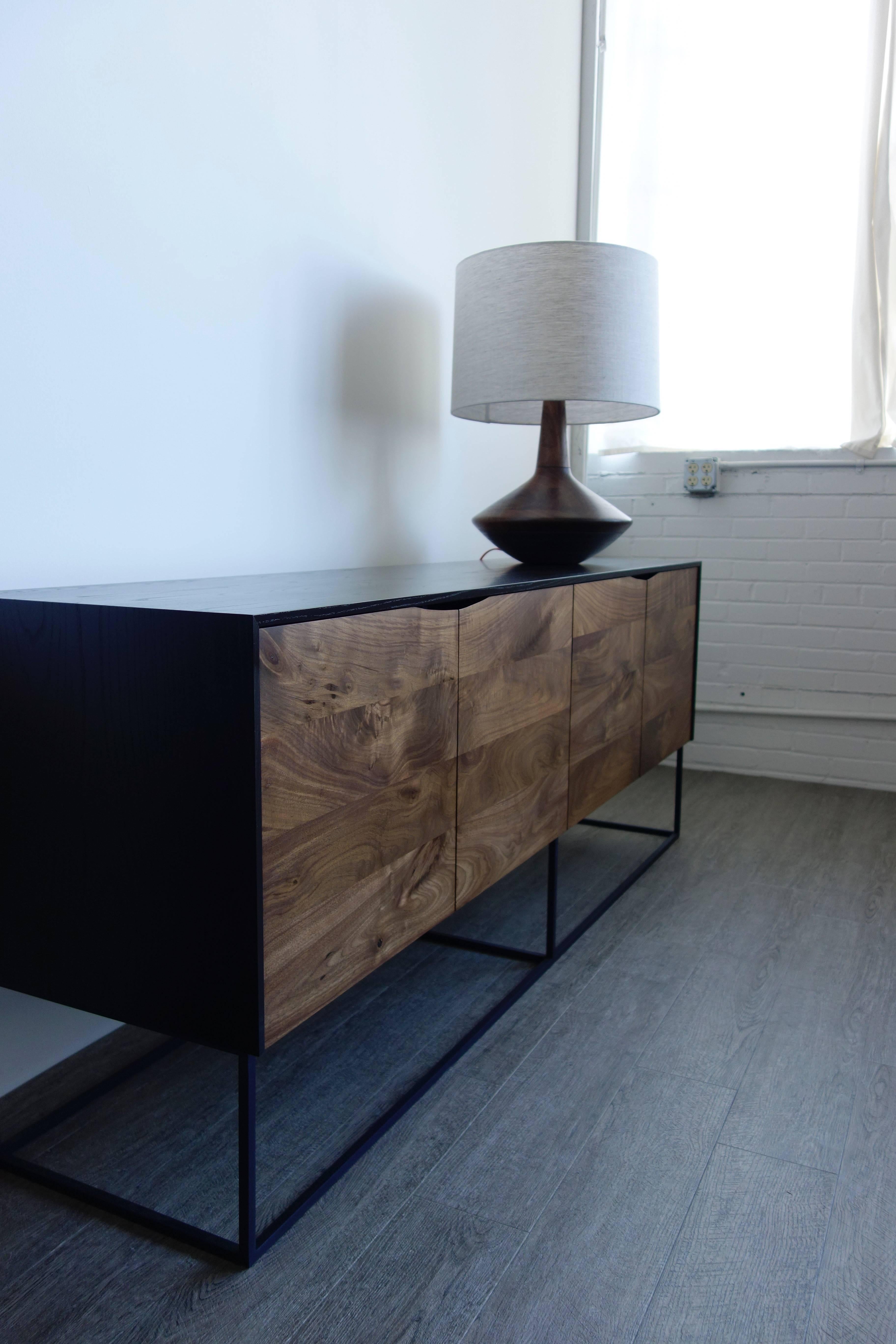 Handcrafted classic modern credenza of ebonized ash and walnut with a cold-rolled steel base. The exterior is ebonized and coated with a durable lacquer; the interior is coated with a proprietary deep blue colored lacquer. The soft-close walnut