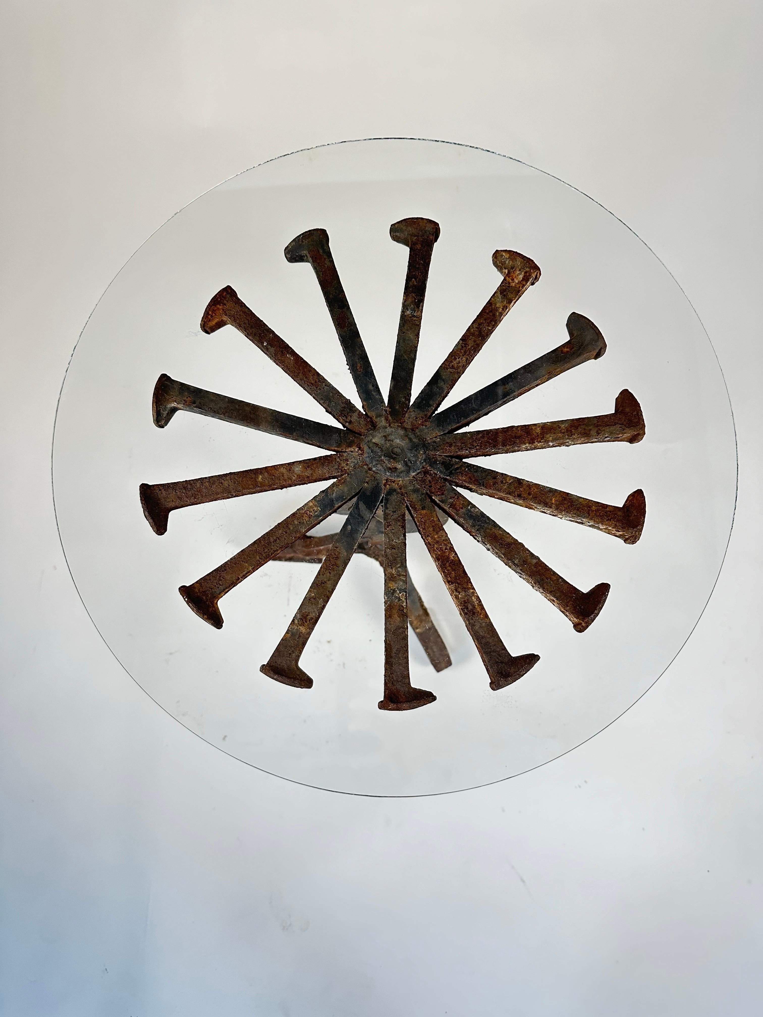Cette table d'appoint unique, faite à la main, est fabriquée à partir de fer forgé, de crampons de chemin de fer réutilisés et de quincaillerie industrielle, ce qui lui confère une présence audacieuse et sculpturale. La base en fer présente une