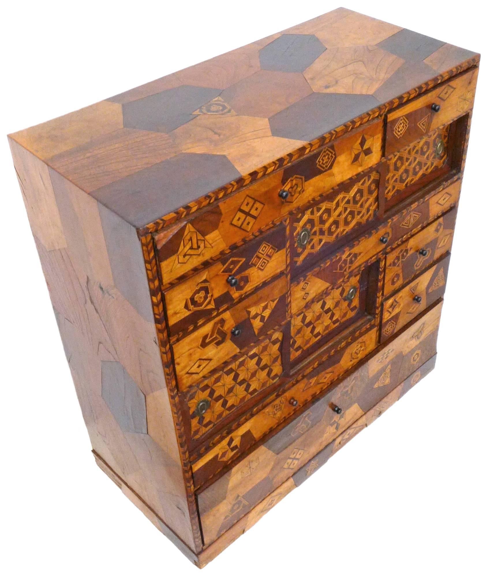A wonderful and unusual handcrafted, Japanese marquetry cabinet. A fantastic, compact piece, thoroughly covered in a playful array of geometric designs; featuring drawers of various sizes as well as sliding-door compartments. Incredible execution