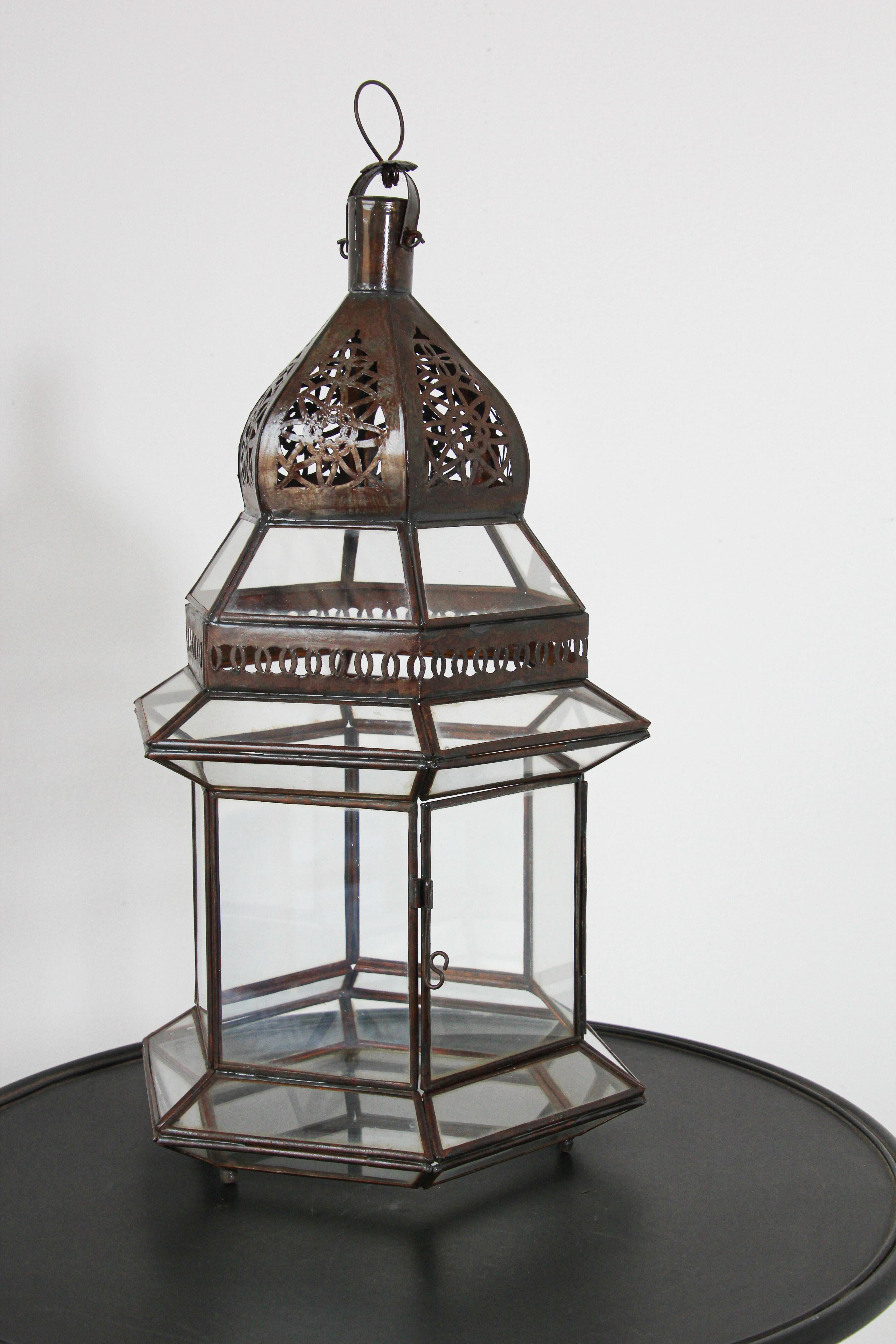 Large Moroccan metal and clear glass lanterns.Hurricane candle lamp in hexagonal shape with vintage rust color metal finish.The top of the lantern is handcut with Moorish designs.The lantern has a small door to access the inside.Many of our