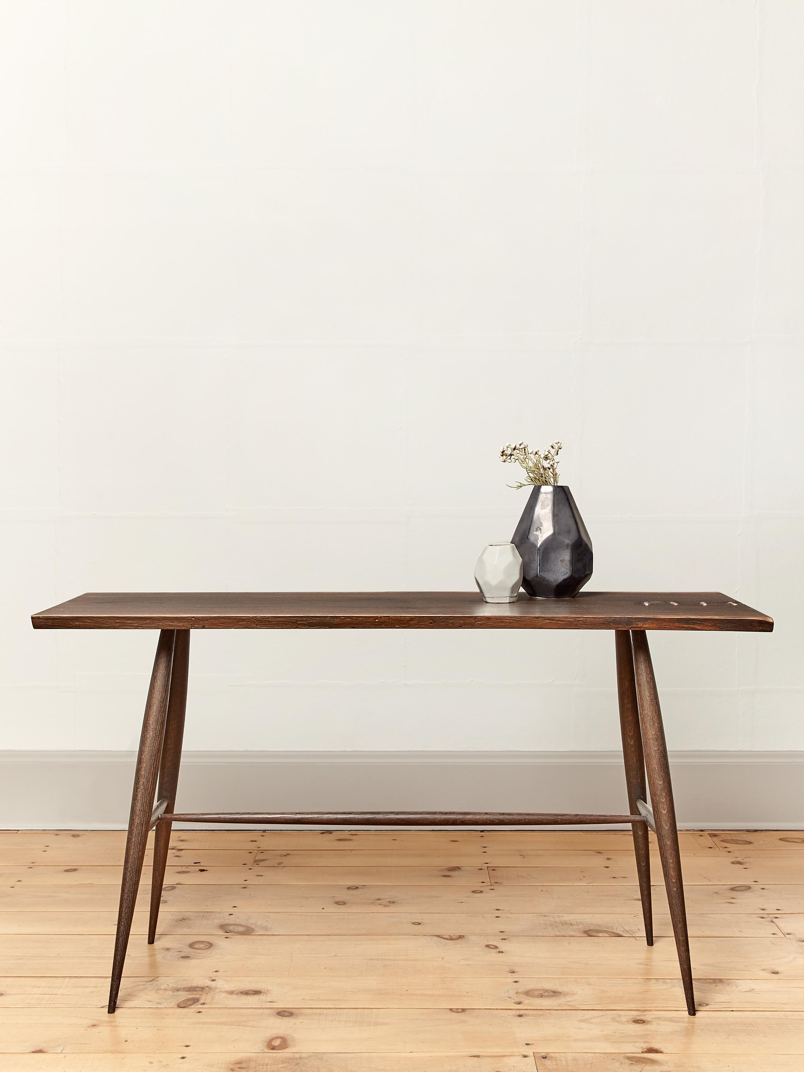 The Devon Mended console features a slender and subtle live edge slab top. Hand hammered copper staples secure the natural cracks in the wood. The slender turned legs and rails are carved to gentle tapers. Naturally oxidized (blackened). Natural oil