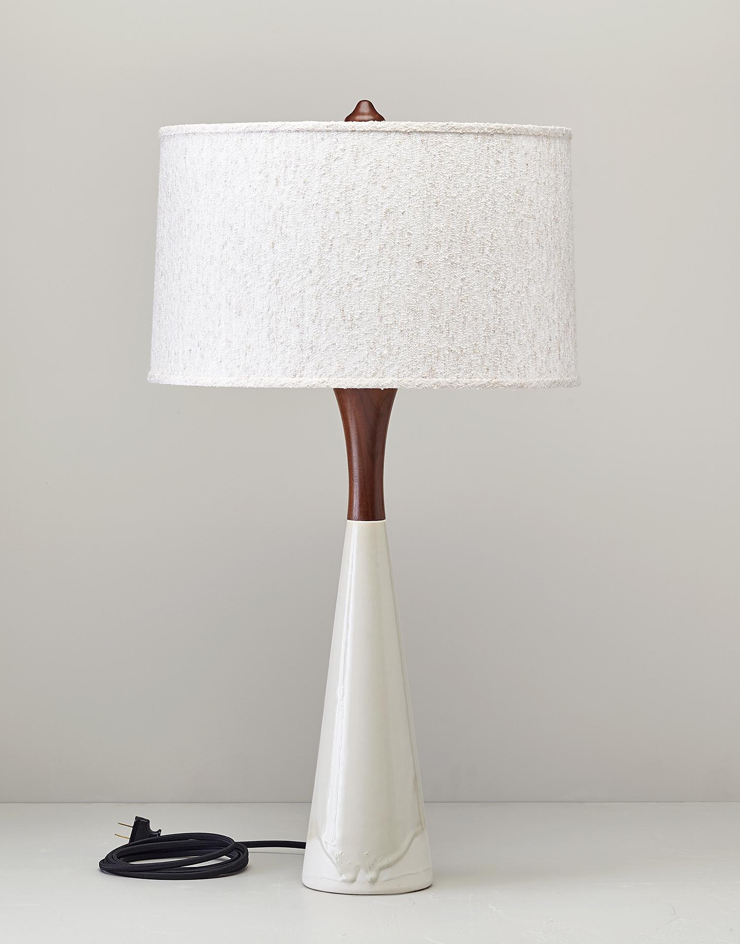 Statuesque Hanni is tall and slender. With a nod to mid-century styling the the handcrafted base is cast in porcelain topped with a turned walnut neck and finial. The shade is made of nubbly boucle. Available in four glazes. Nickel hardware.