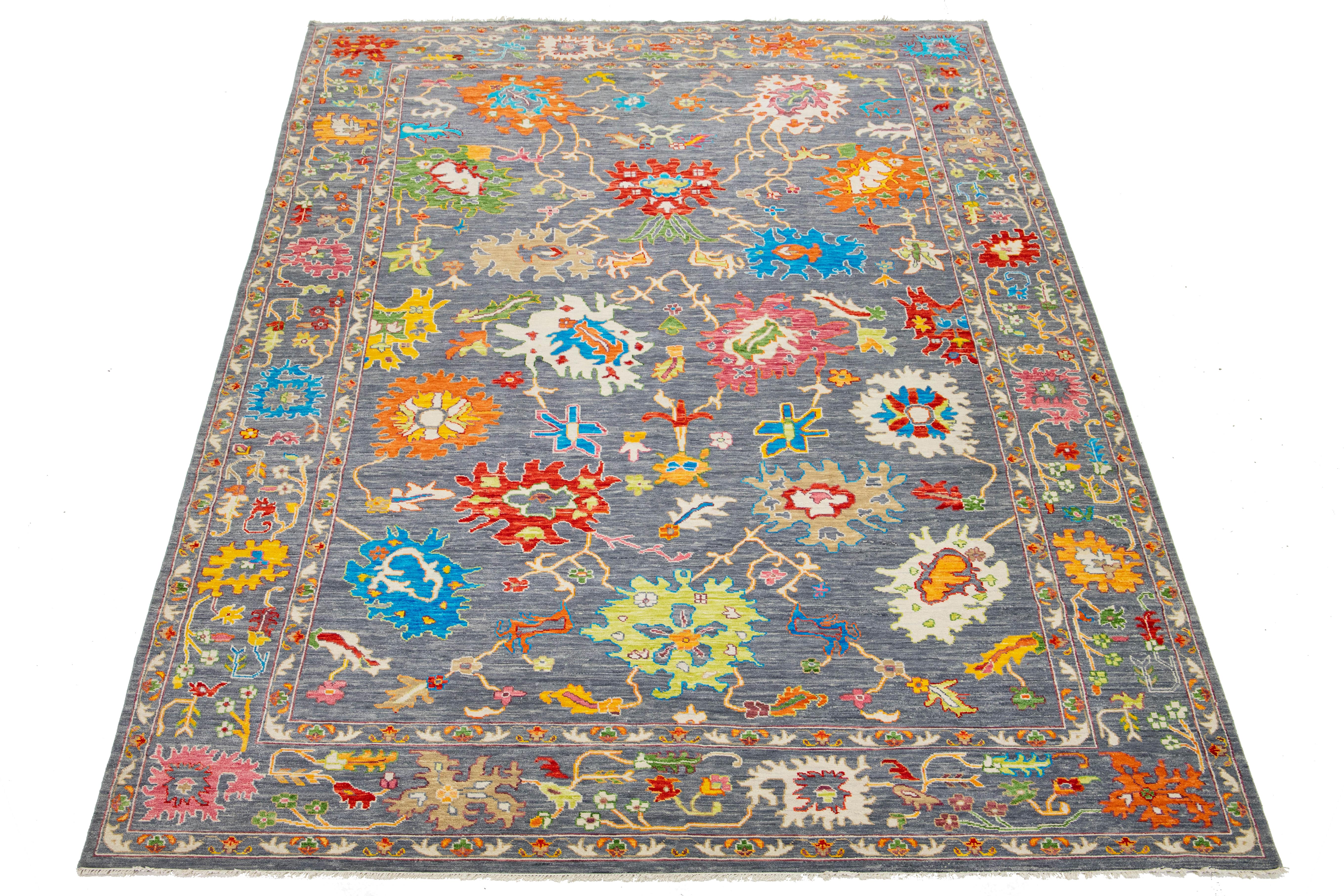This modern Oushak-style wool rug seamlessly blends contemporary style with the timeless charm of traditional Oushak design. It features a striking gray background adorned with vibrant floral patterns in a captivating array of colors that draw