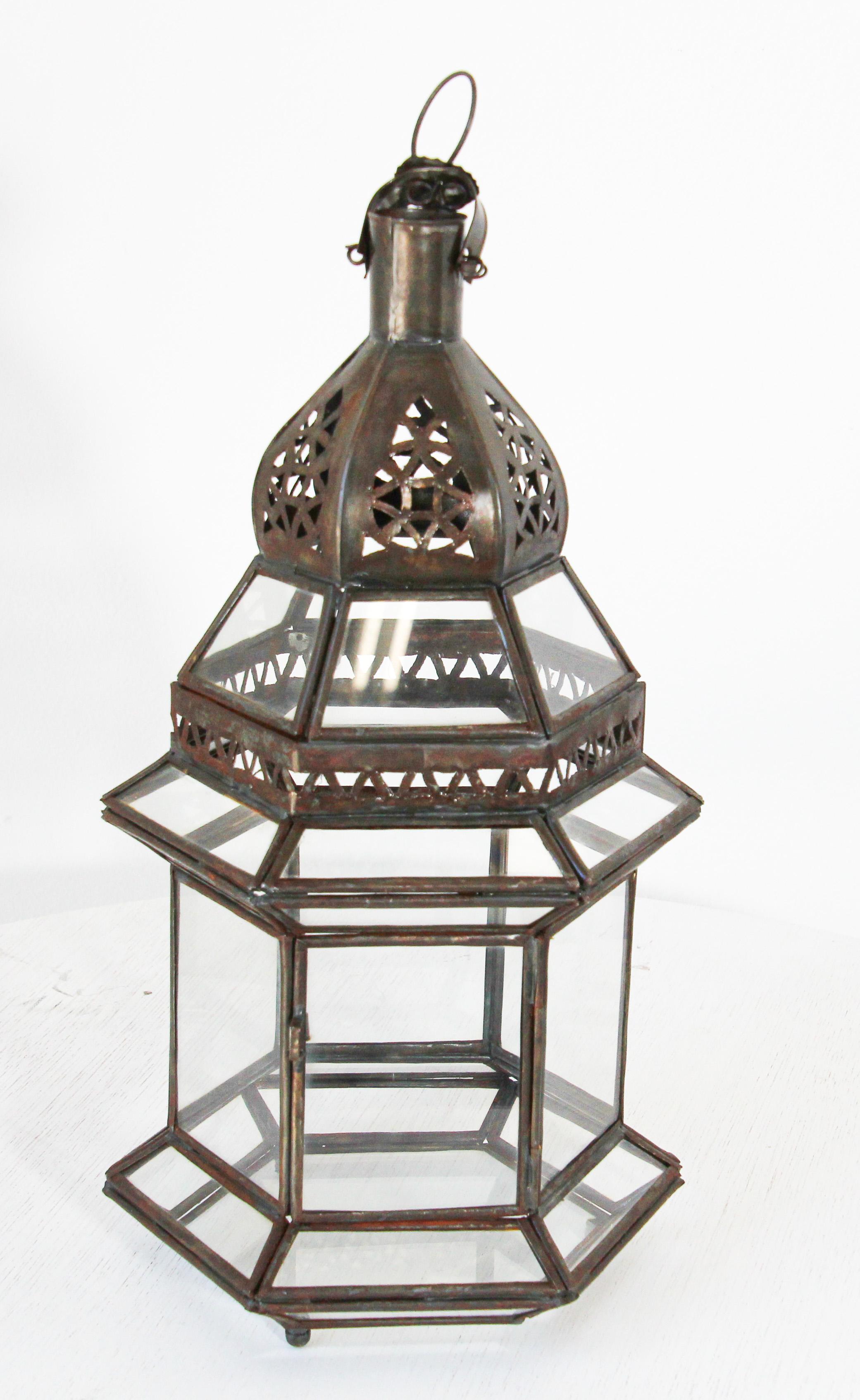 Moroccan metal and clear glass lanterns.
Hurricane candle lamp in hexagonal shape with vintage rust color metal finish.
The top of the lantern is hand-cut with Moorish designs.
The lantern has a small door to access the inside. 
Many of our