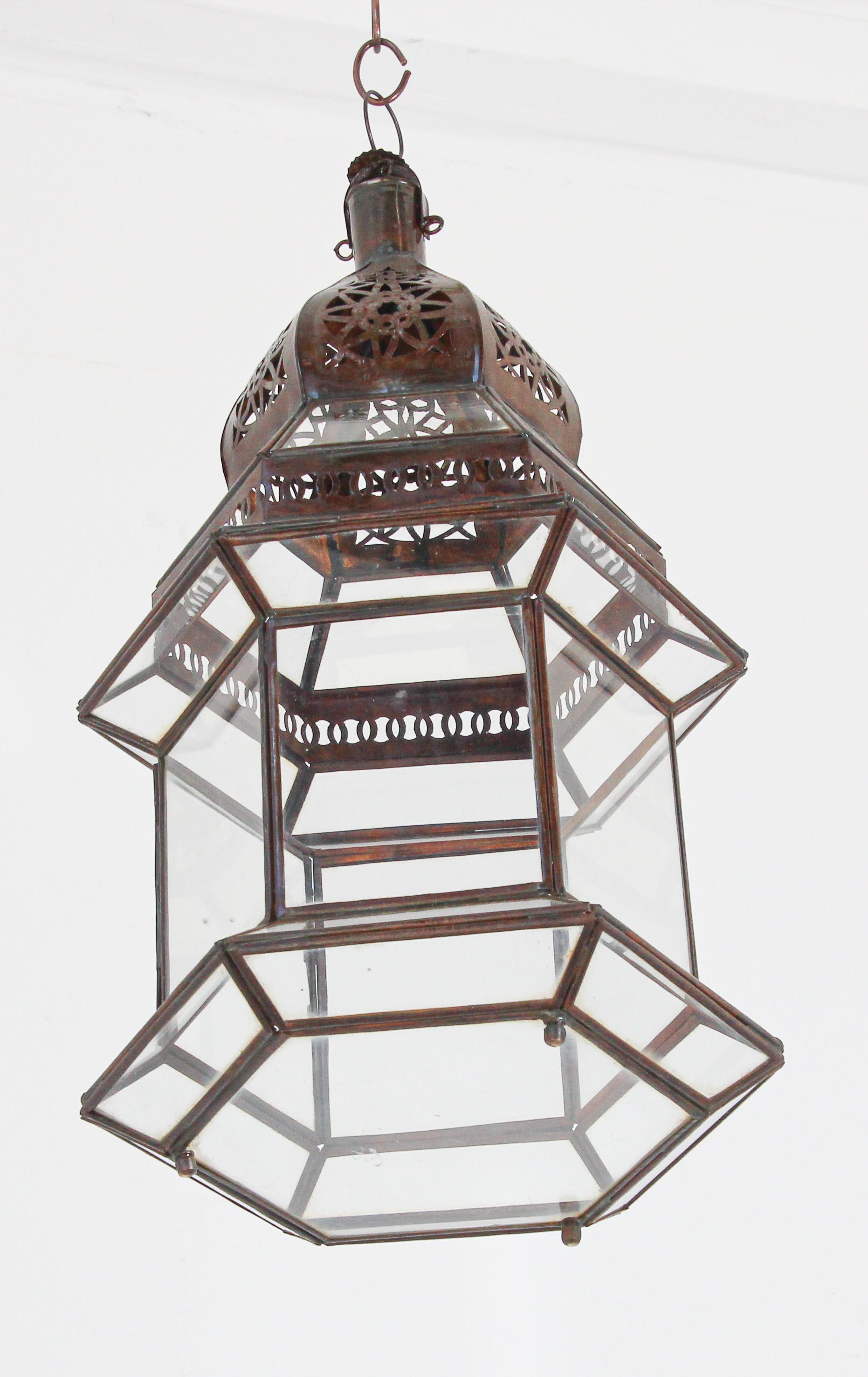 Moroccan metal and clear glass hanging candle lantern.
Hurricane candle lamp in hexagonal shape with vintage rust color metal finish.
The top of the lantern is hand-cut with Moorish designs.
The lantern has a small door to access the inside to use