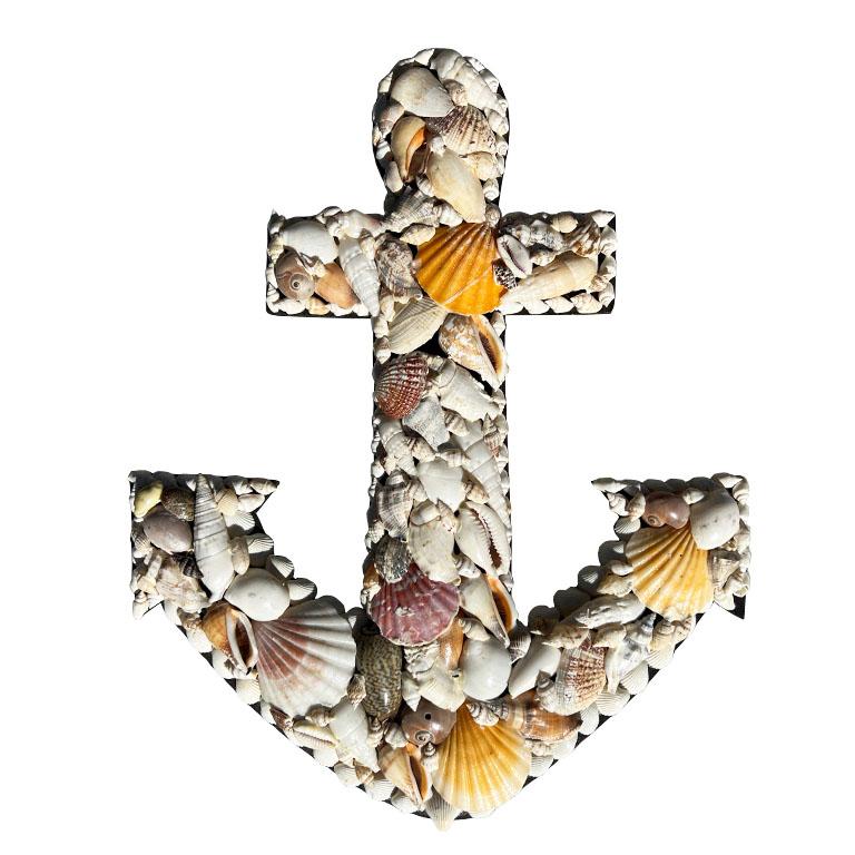 A natural hand-crafted sea shell encrusted anchor wall hanging. Created from wood, this piece is in the shape of a boat anchor, and features applied natural sea shells of all colors. The edges are lined with crisp white cockle shells and Babylon