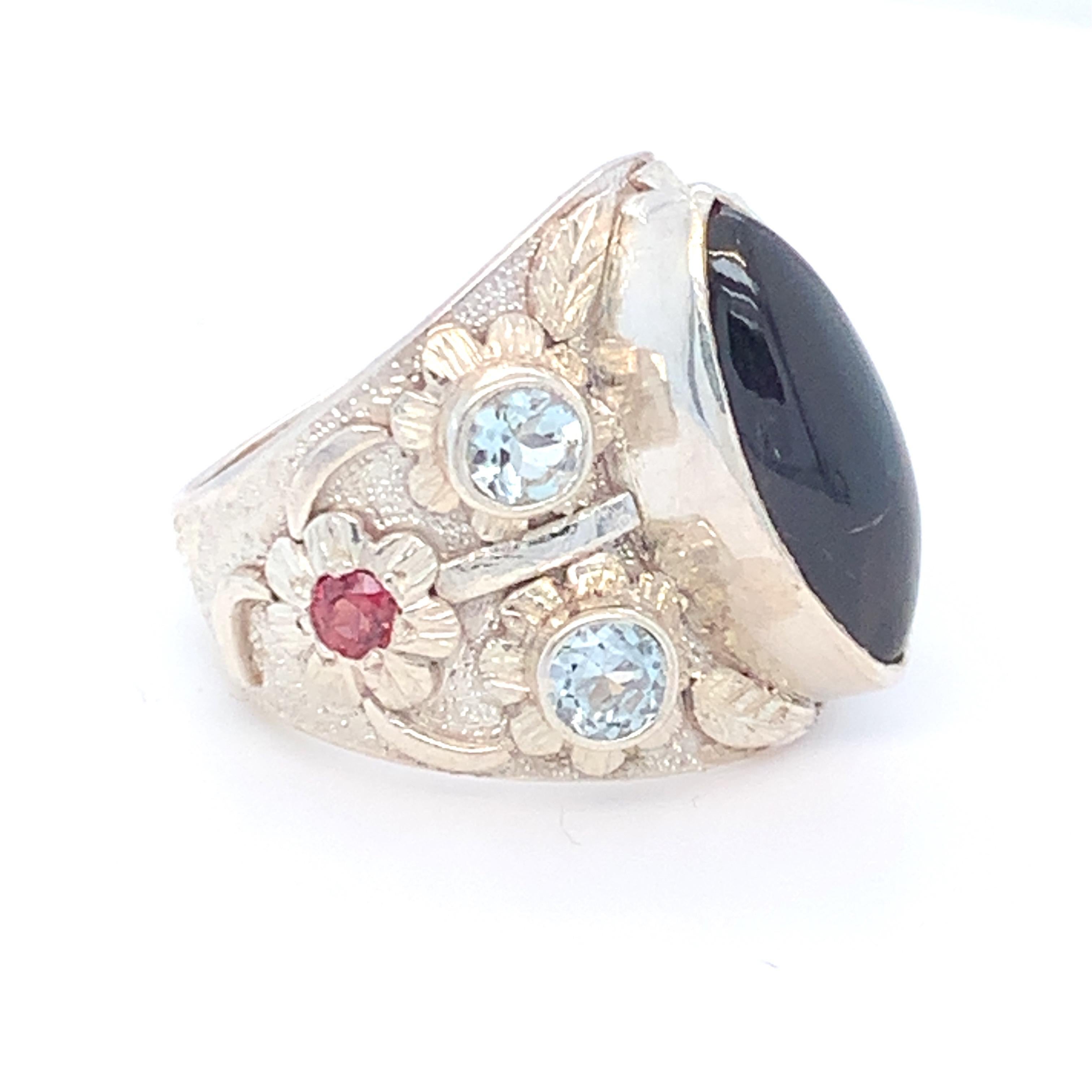 Marquise cabochon  Iolite is the center stone with symmetrical settings of round aquamarine and Tourmaline  on both sides of this stunning, one of a kind cocktail ring. Floral motifs on the sides gives it a feminine touch. Set in sterling silver and