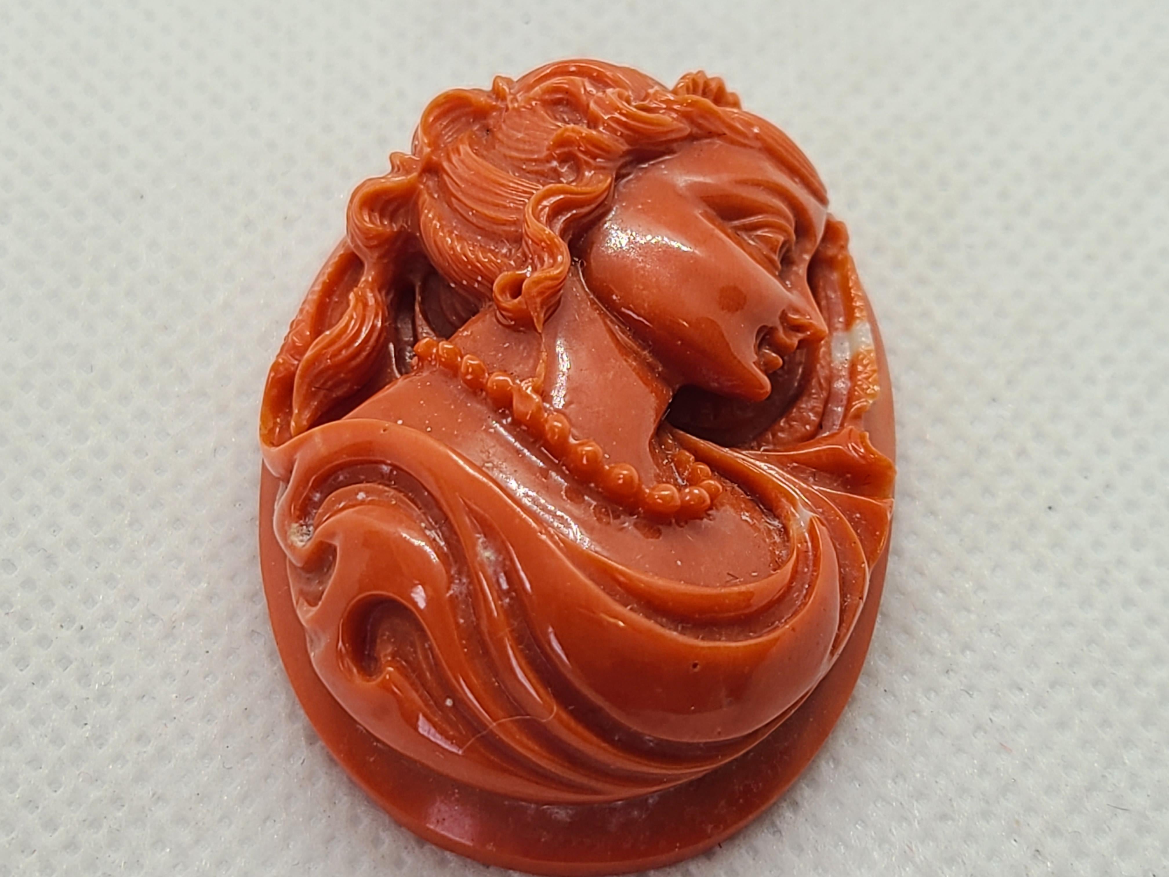 Cet ornement exquis est composé de corail naturel rouge-orange, sculpté de façon complexe en un portrait de femme finement détaillé. Mesurant environ 4,4 x 3,2 x 1,5 cm, il est le fruit d'un travail de maître, idéal pour les collectionneurs, les