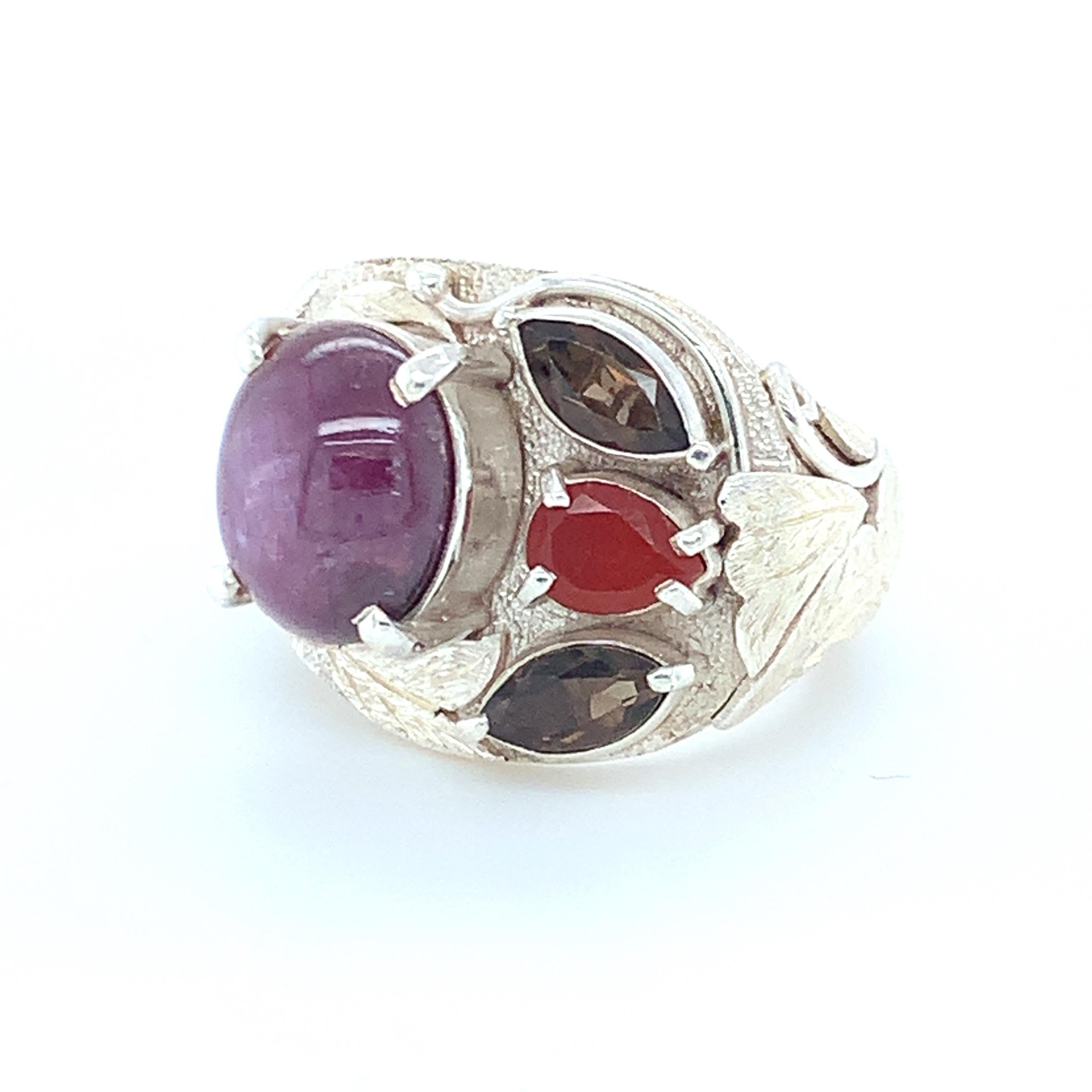 Round cabochon cut star ruby is the main stone along with smoky topaz and orange onyx which are set in asymmetric design. Multi-layer work on the sides enhances the beauty of this ring. Set in sterling silver and carefully crafted with hand makes it