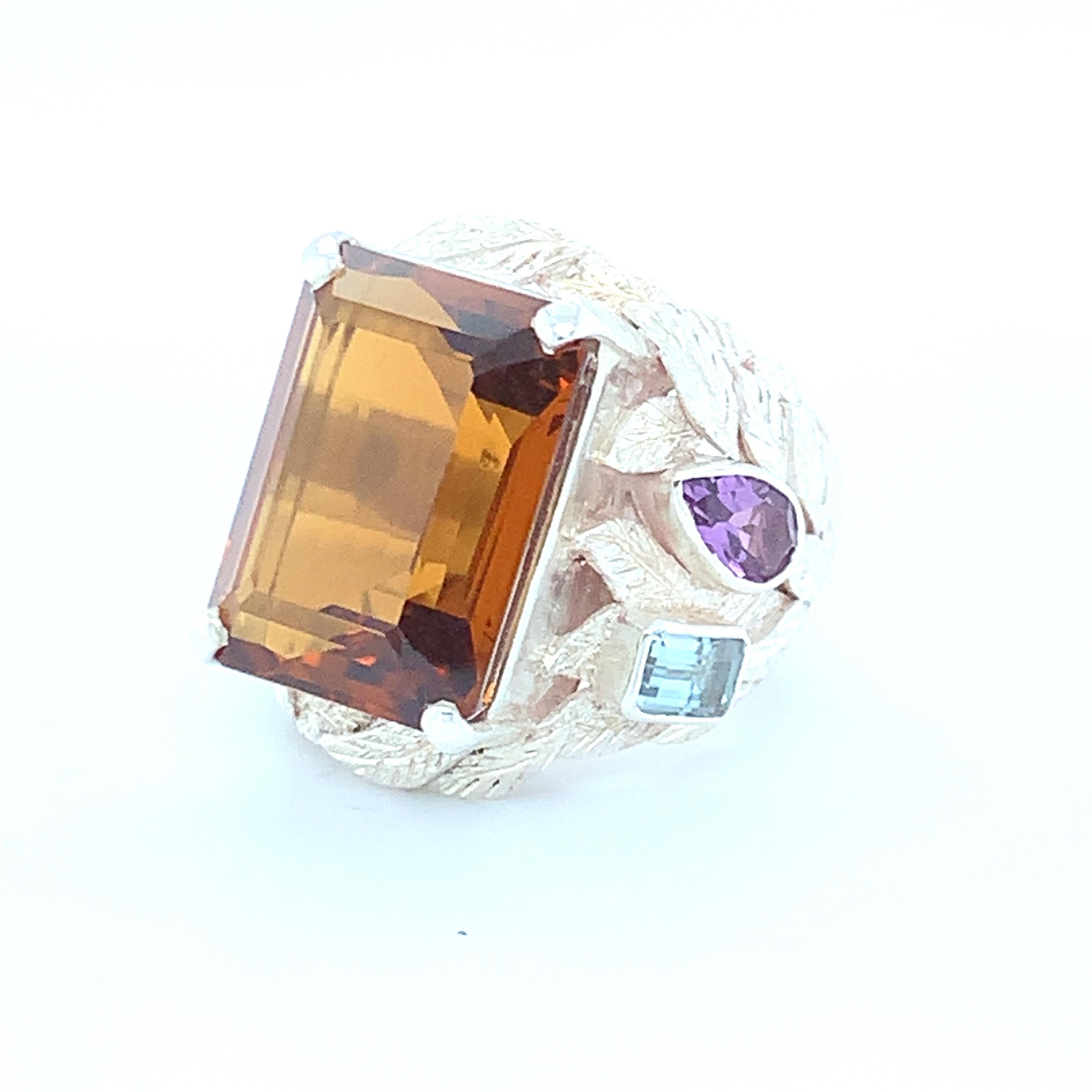 Huge emerald cut Brandy Topaz is the center stone of this stunning, one of a kind cocktail ring. Accents of amethyst and aquamarine are on both sides which enhances the beauty of this ring which is Set in sterling silver and carefully crafted with