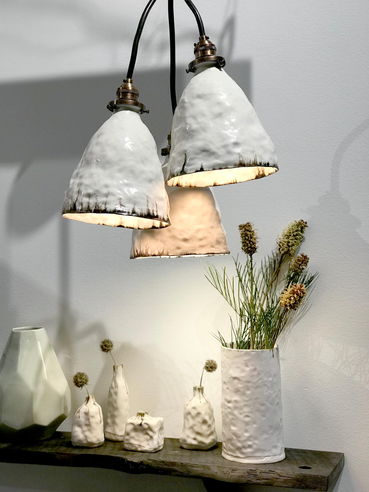 We've combined the comfort of rustic forms in porcelain with the industrial vibe of antiqued bronze elements to create a unique pendant light. The three porcelain shades are hand cast in porcelain, glazed in either warm white snowflake glaze and