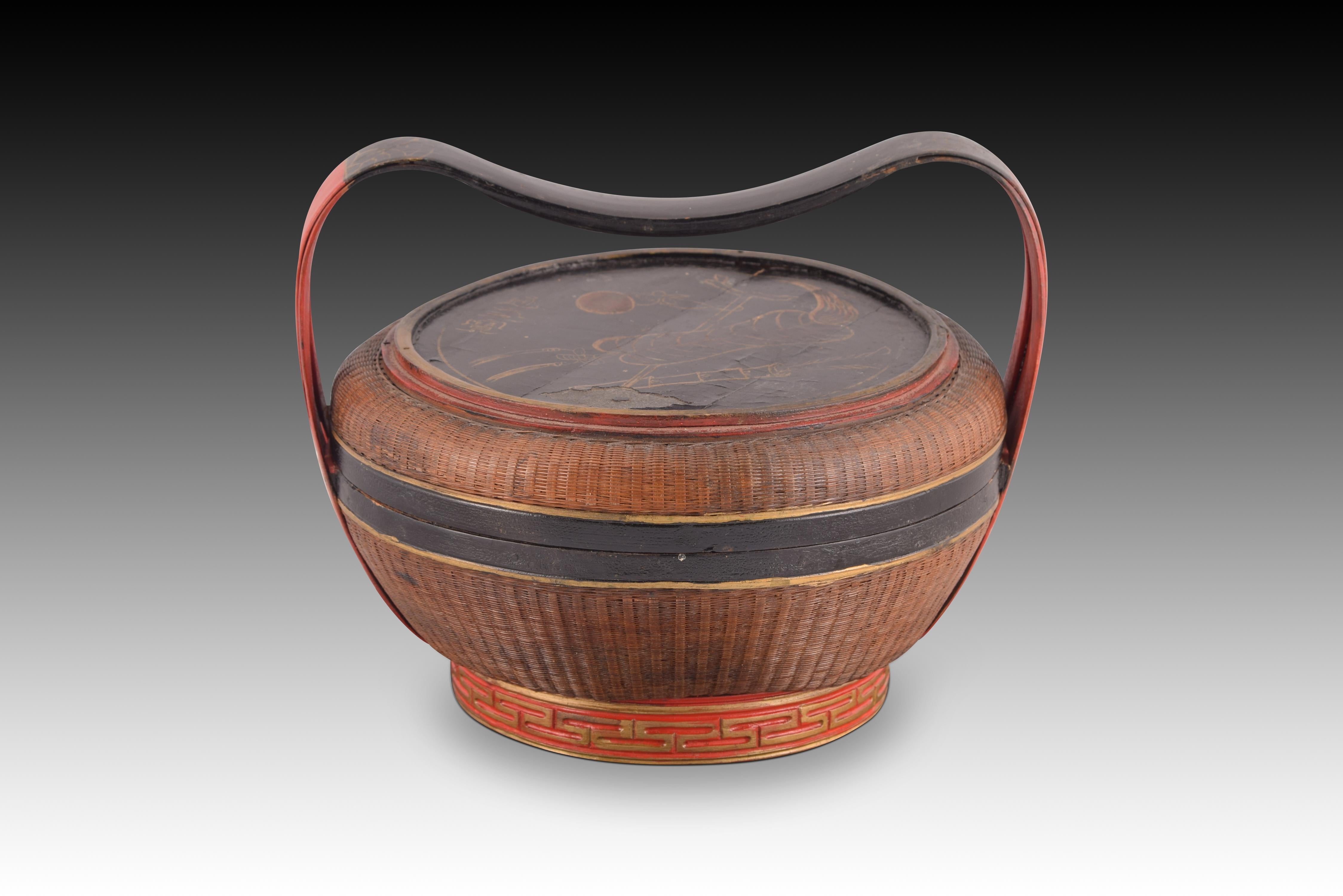 Handcrafted oriental basket. Vegetal fibers. Around 1950.
 Basket with a circular base (decorated with a fine gold fretwork relief) that has a curved handle and polychrome areas in red and black; The cover presents a figurative composition (fan on a