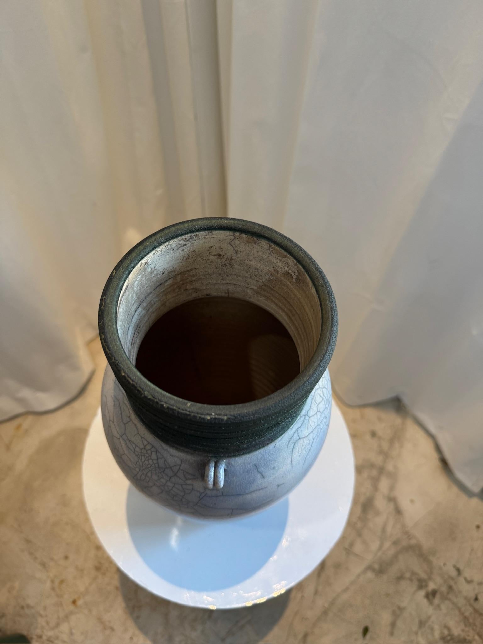 Questo vaso in ceramica Raku realizzato a mano è un'accattivante miscela di arte tradizionale e texture organica. La superficie è caratterizzata da un'intricata smaltatura a crepe, ottenuta con l'antica tecnica di cottura giapponese Raku, che crea