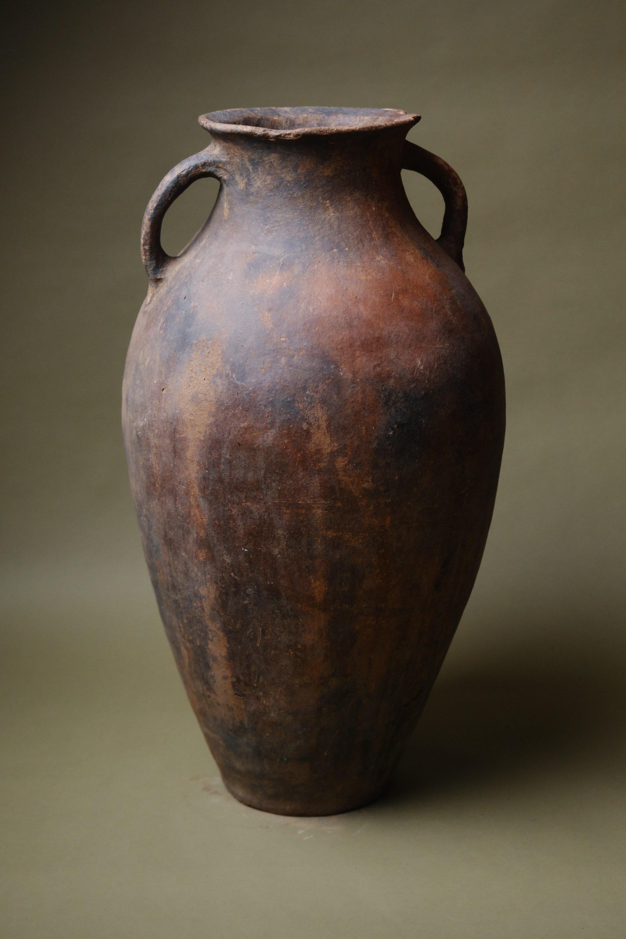 Ti presentiamo l'Amphora di terracotta lavorata a mano, un pezzo che incarna l'essenza dell'artigianato mediterraneo e del fascino rustico. Quest'anfora, tradizionalmente utilizzata per conservare prodotti essenziali come l'olio d'oliva e i cereali,