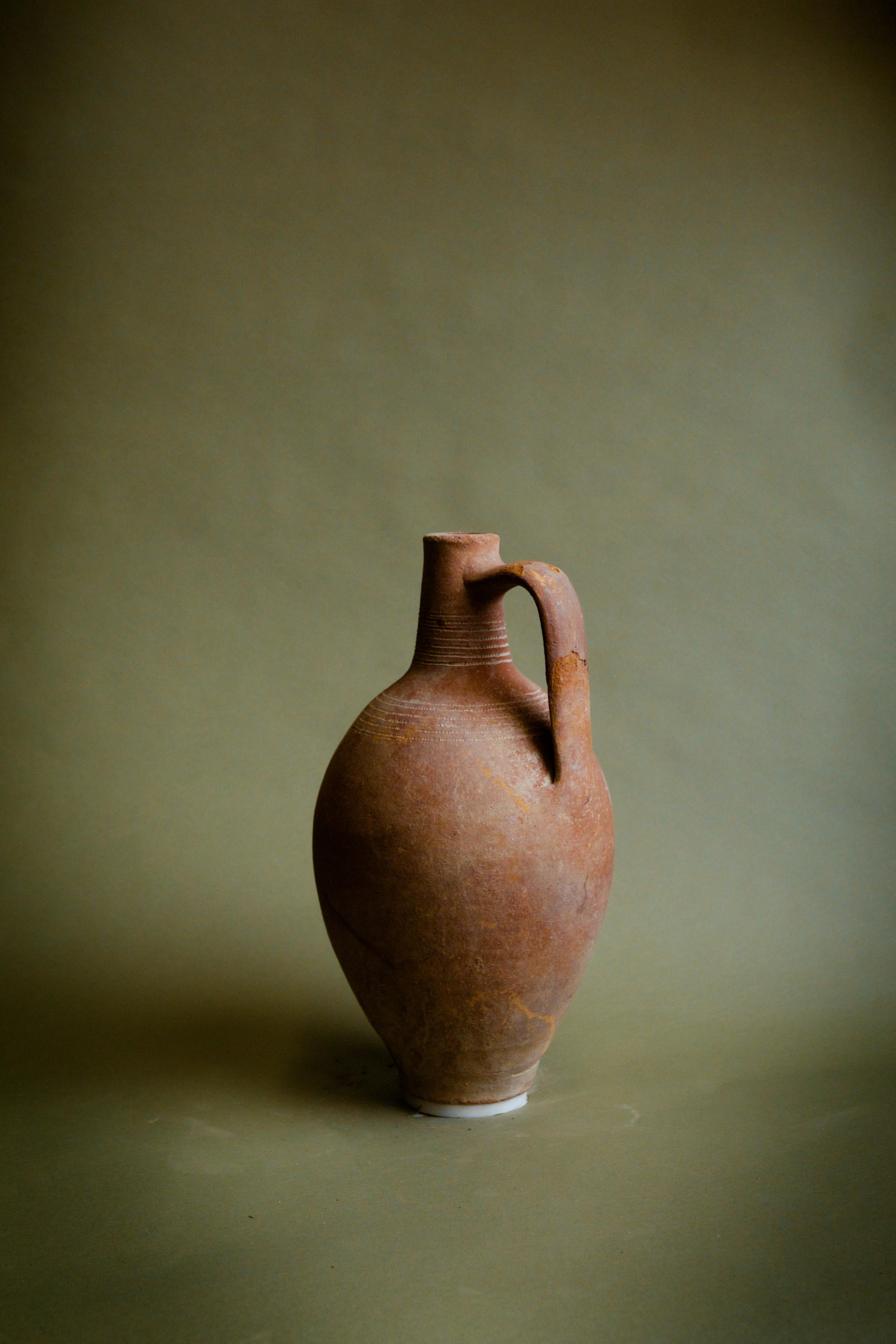 Disfruta de la elegancia atemporal de esta Jarra de Anatolia de asa fina, una vasija turca de barro de época, fabricada en el siglo XX. Esta pieza expertamente moldeada a mano presenta un asa graciosamente alargada, que pone de relieve la habilidad