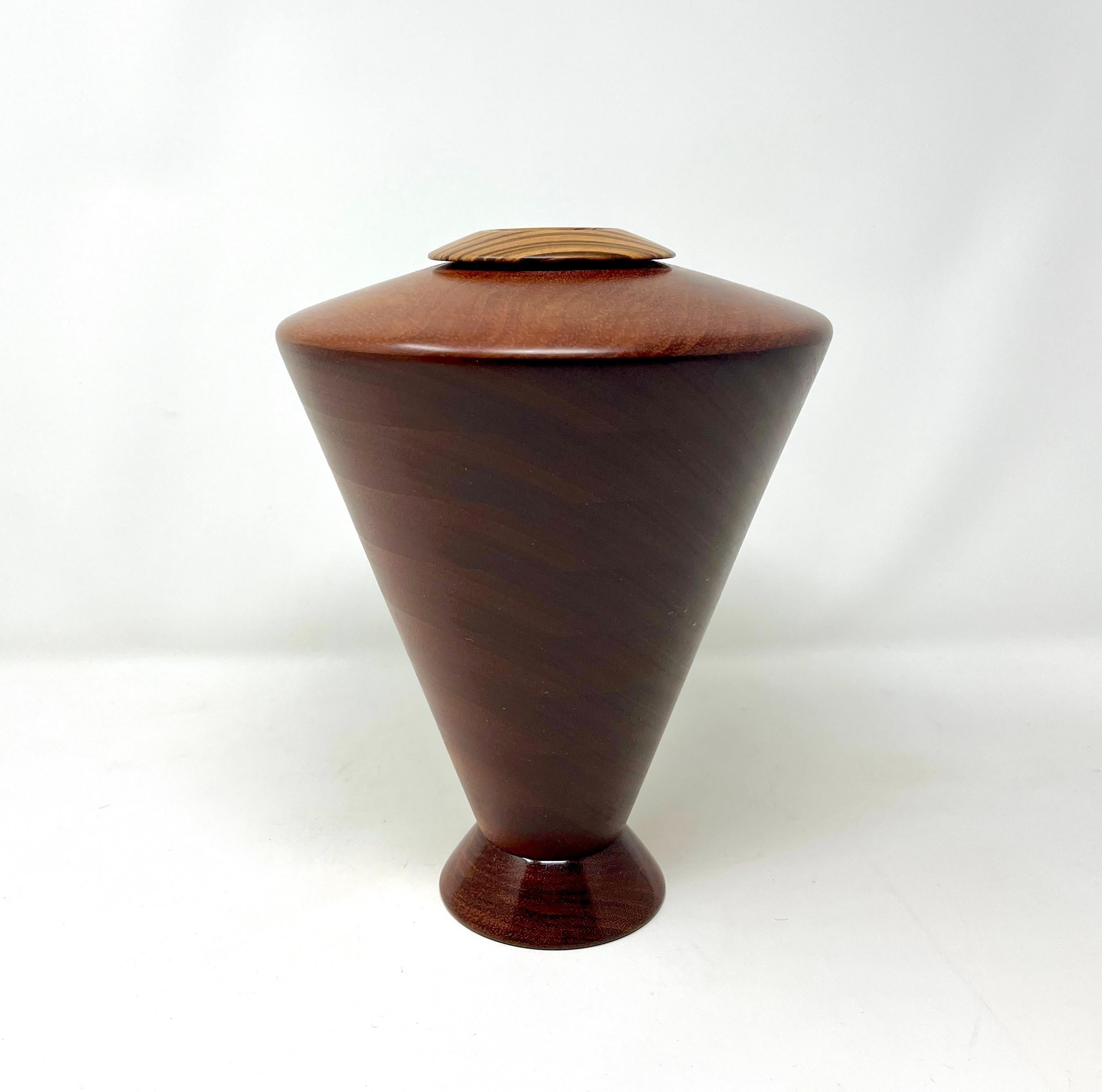 Beautiful example of late 20th/21st century American craftsman Lloyd Cheney who mastered the art of making wood vessels on a ringmaster. Made in 2002, signed and penny stamped, this turned wood vessel features a striking zebra wood rim atop an