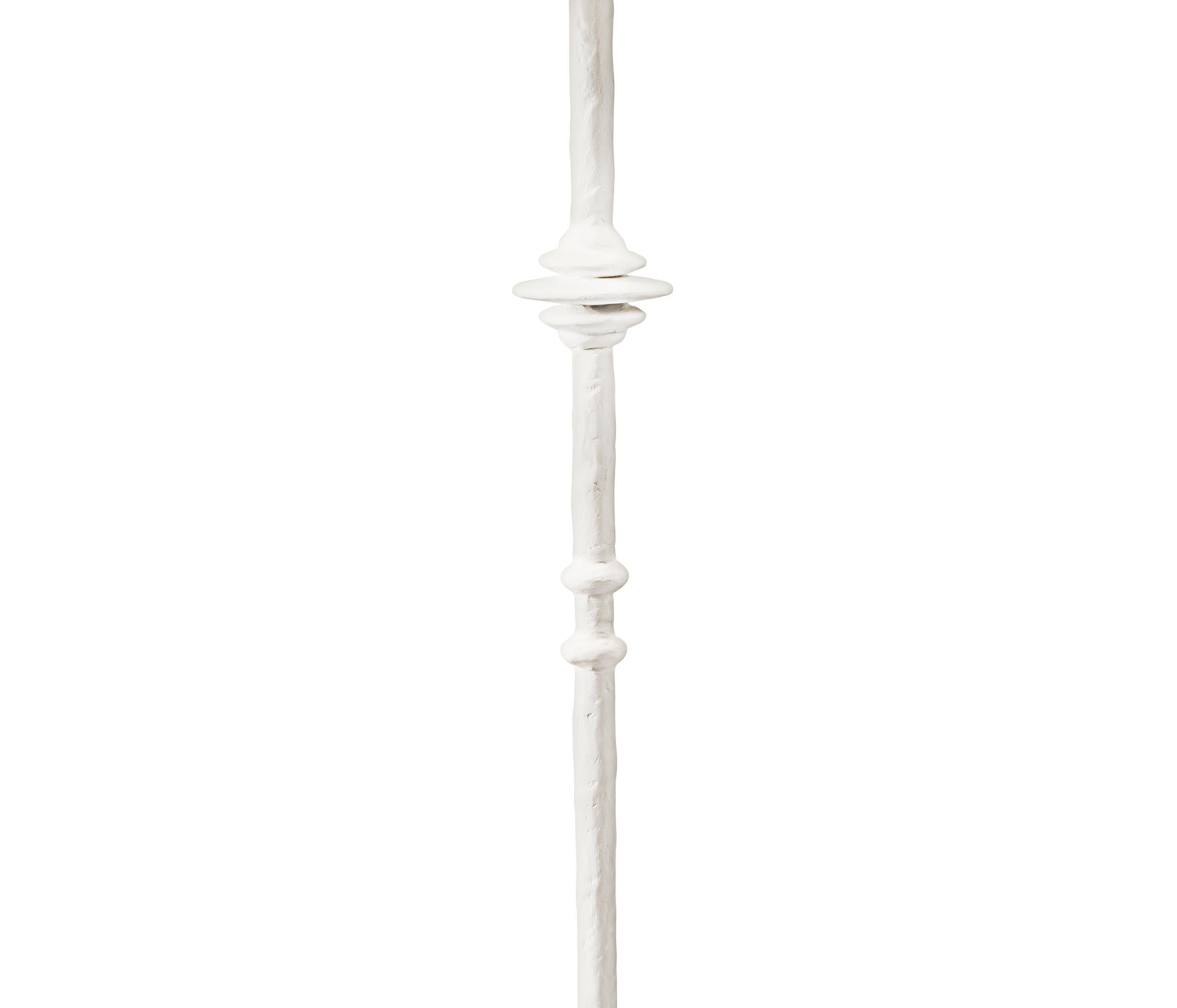 Le lampadaire Mittis évoque les pièces en bronze texturé conçues par les frères Giacometti. Le minimalisme simple de cette lampe est adouci et transformé par la texture brossée du plâtre sculpté. Des détails comme les pieds et les anneaux en forme