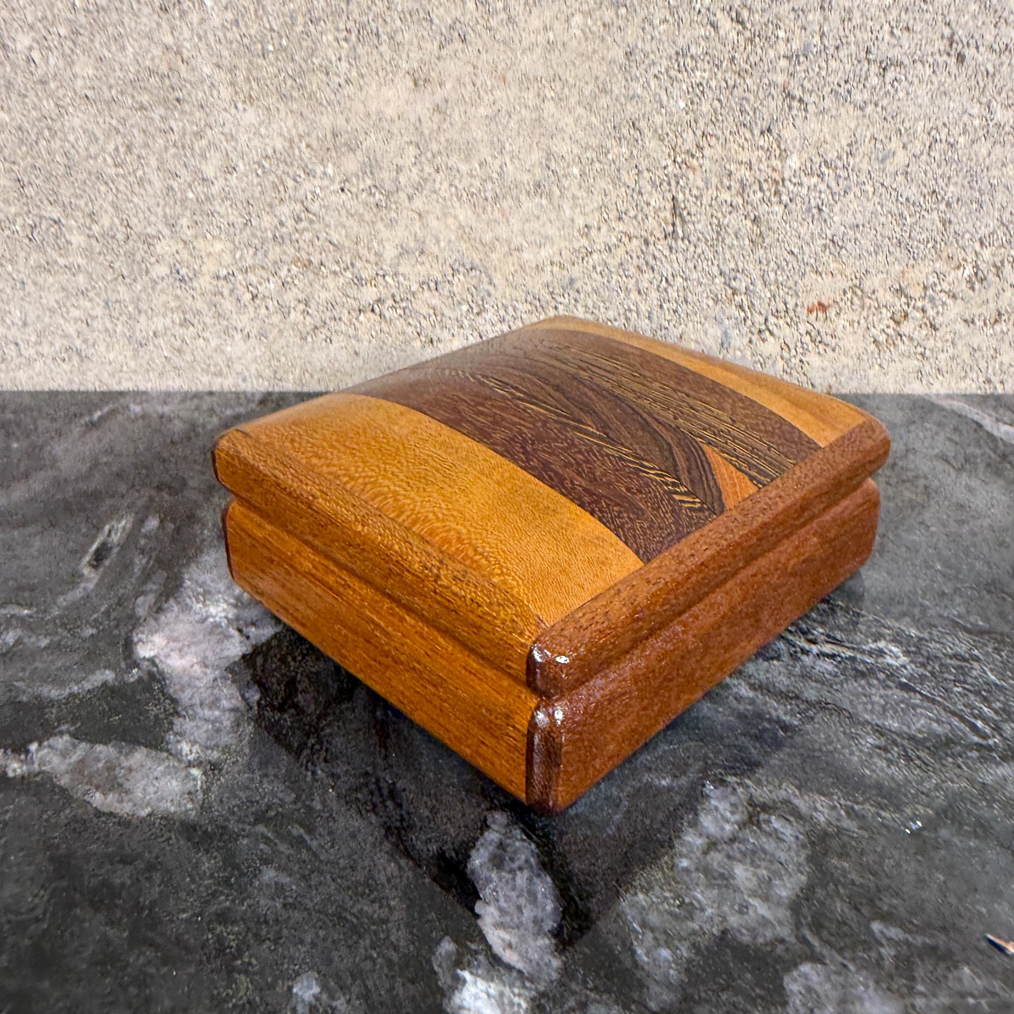 Nous vous proposons une petite boîte en bois fabriquée à la main, probablement une boîte à bijoux ou à souvenirs, dotée d'un couvercle bombé et de différentes essences de bois. 
La boîte présente une finition polie qui met en valeur les variations