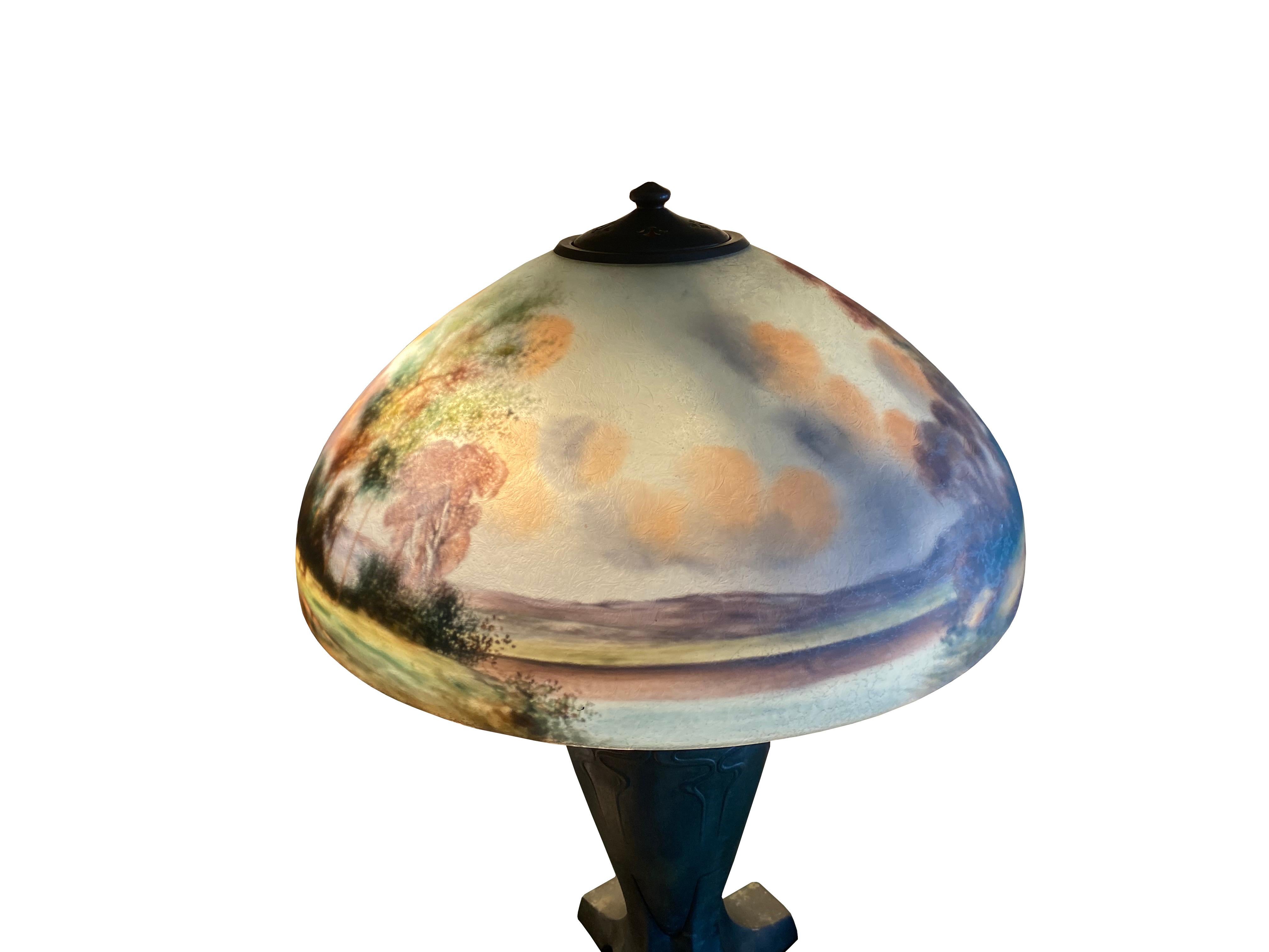 A Handel patinated metal table lamp with reverse painted glass shade depicting a woodland landscape,
first quarter of the 20th century
Side of foot to base inscribed HANDEL, shade inscribed HANDEL and artist signed John Baily,
Measures: Diameter